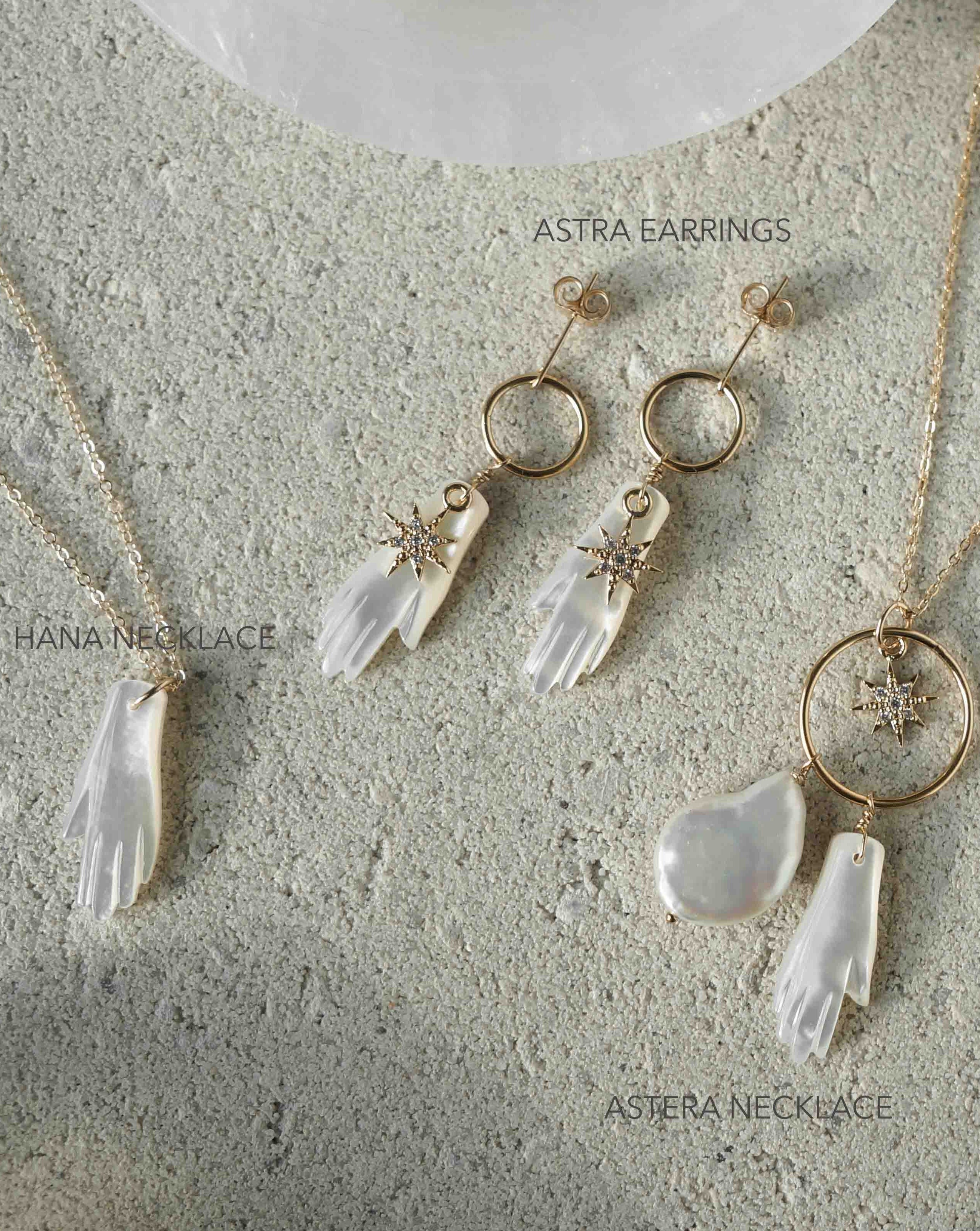 Astra Earrings by KOZAKH. Dangling earrings in 14K Gold Filled, featuring a hand carved Mother of Pearl hand charm and a Cubic Zirconia star charm.