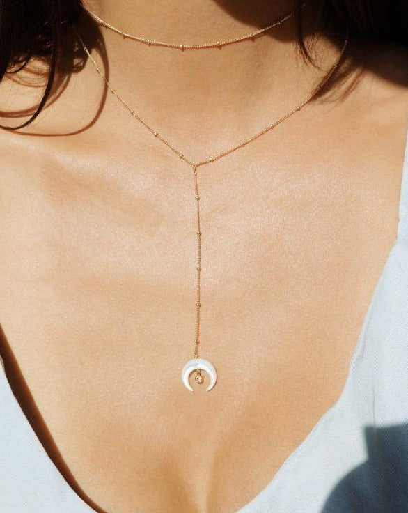 Baque Lar Necklace by KOZAKH. A 16 to 18 inch adjustable length, 3 inches chain drop lariat style necklace in 14K Gold Filled, featuring a hand-carved Mother of Pearl moon charm and a 2mm Swarovski Crystal.
