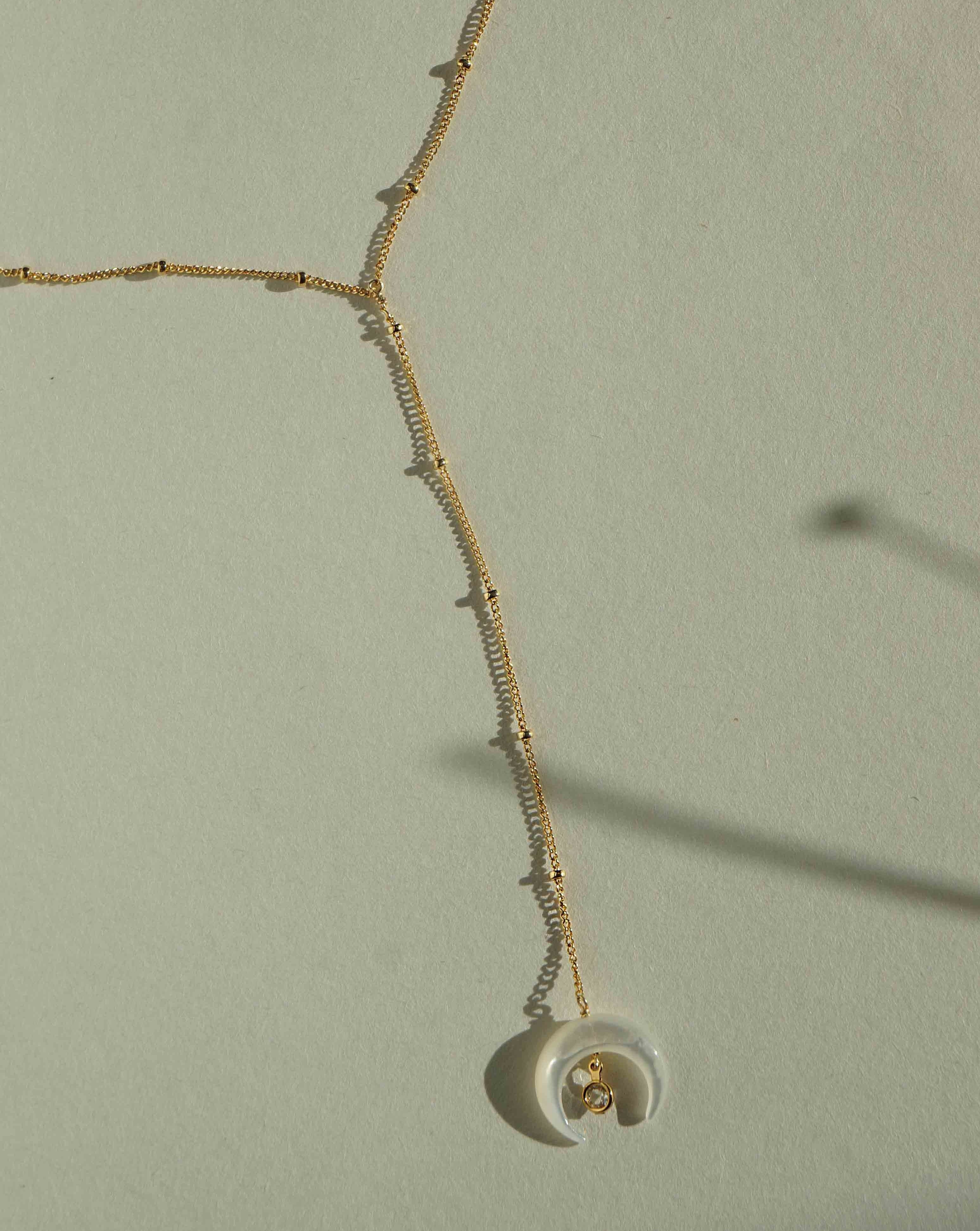 Baque Lar Necklace by KOZAKH. A 16 to 18 inch adjustable length, 3 inches chain drop lariat style necklace in 14K Gold Filled, featuring a hand-carved Mother of Pearl moon charm and a 2mm Swarovski Crystal.