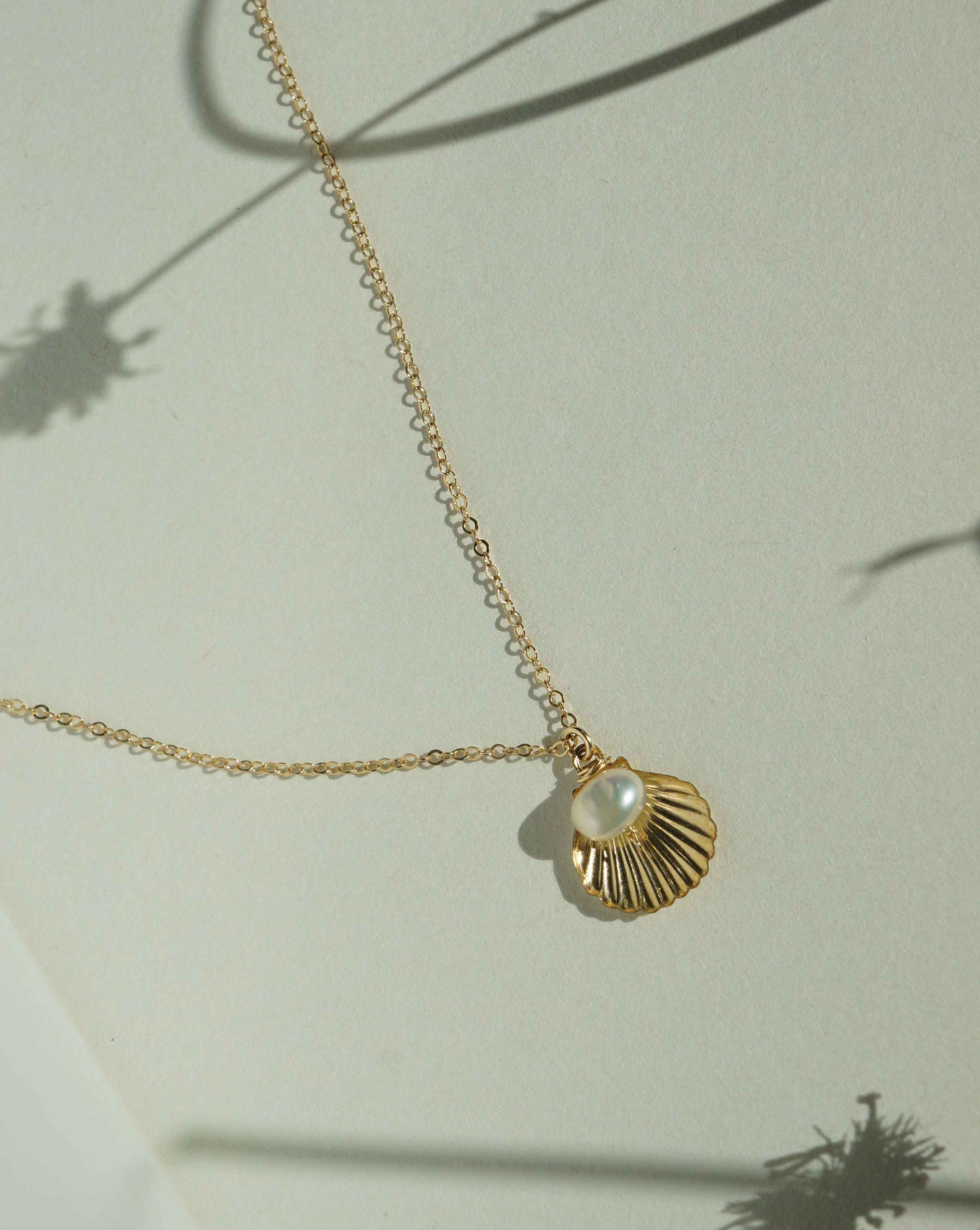 Belle Necklace by KOZAKH. A 16 to 18 inch adjustable length necklace in 14K Gold Filled, featuring a 5mm flat irregular Pearl and a Shell charm.