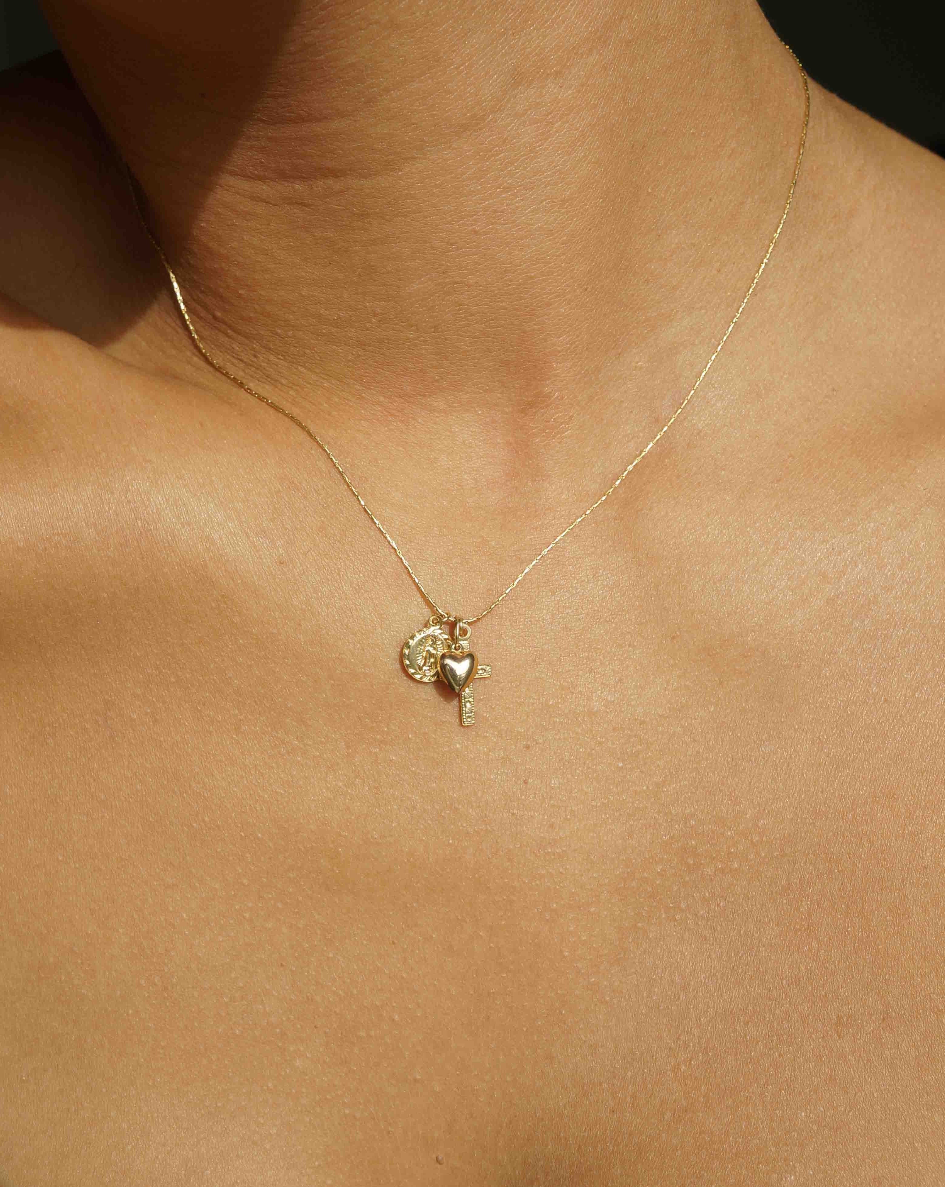 Domingo Necklace by KOZAKH. A 16 to 18 inch adjustable length necklace in 14K Gold Filled, featuring a Saint Christopher medallion, a 6mm Heart charm, and a Filigree decorated cross.