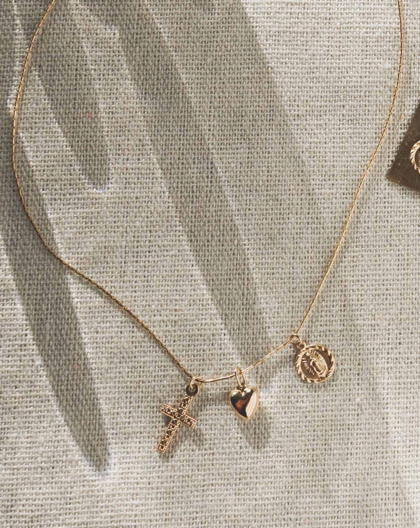 Domingo Necklace by KOZAKH. A 16 to 18 inch adjustable length necklace in 14K Gold Filled, featuring a Saint Christopher medallion, a 6mm Heart charm, and a Filigree decorated cross.