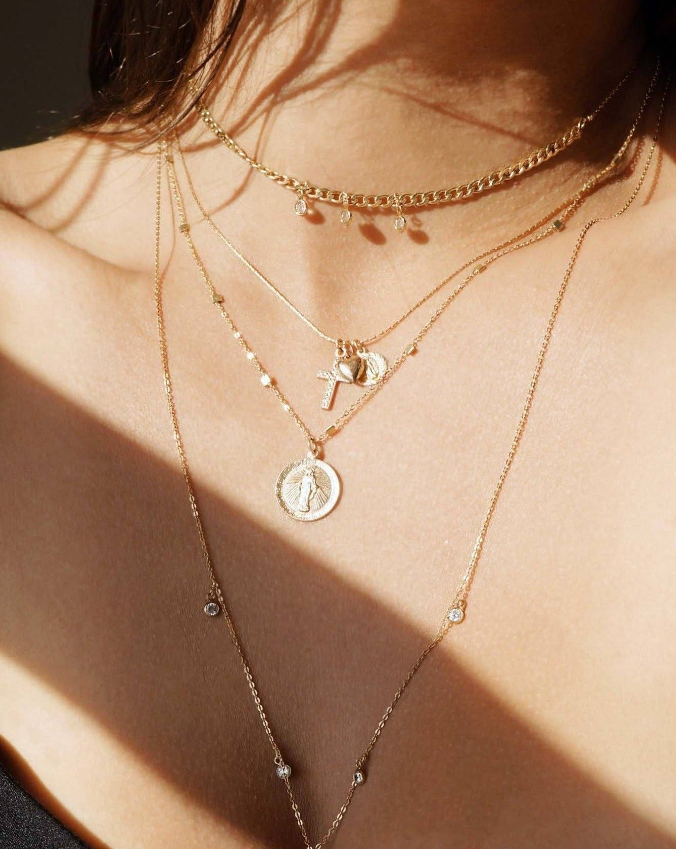 Domingo Necklace by KOZAKH. A 16 to 18 inch adjustable length necklace in 14K Gold Filled, featuring a Saint Christopher medallion, a 6mm Heart charm, and a Filigree decorated cross.