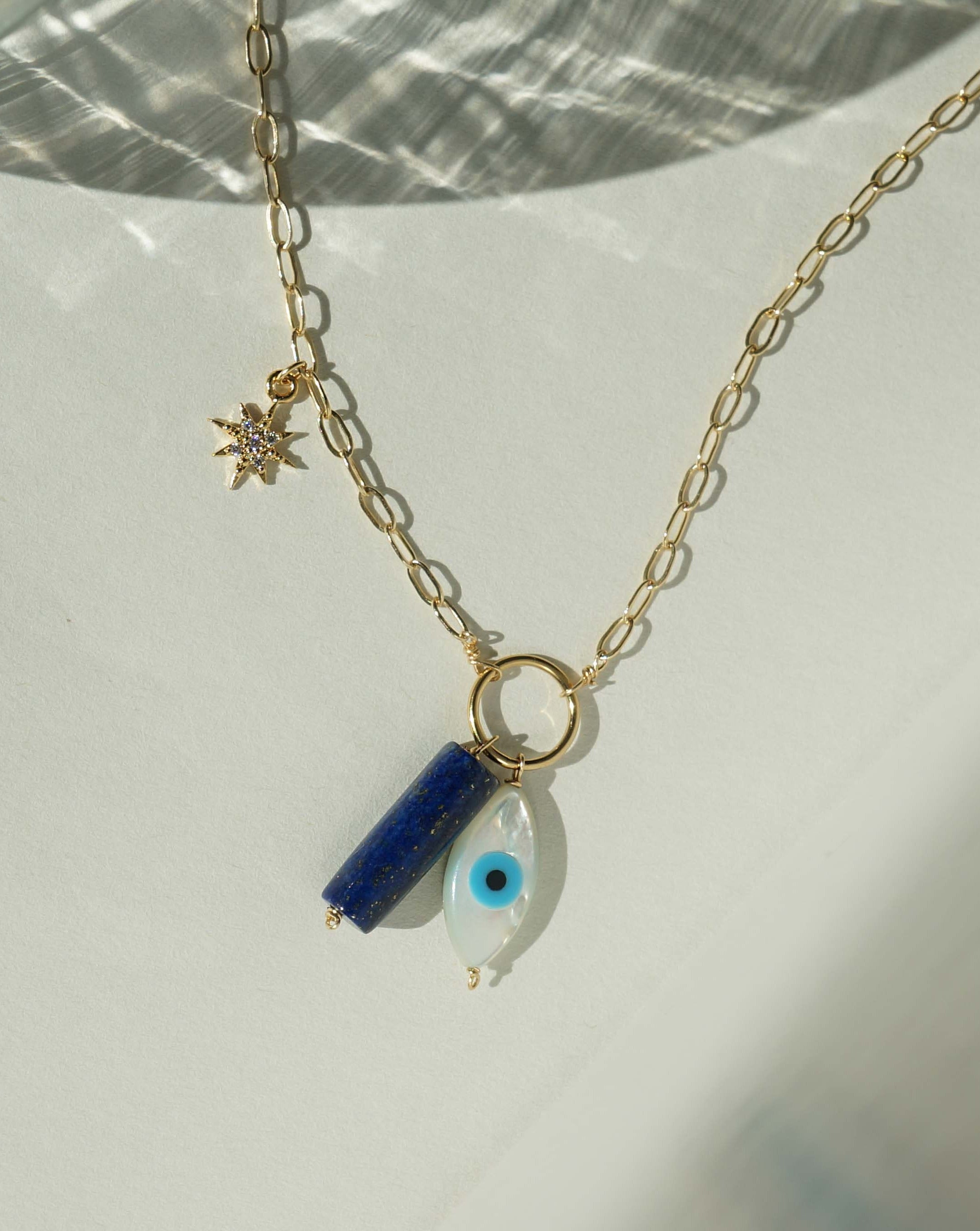 Eye Chakra Necklace by KOZAKH. A 14K Gold Filled necklace with adjustable length from 20 inches, featuring a hand carved Mother of Pearl Evil Eye, a cylindrical cut Lapis, and a Cubic Zirconia encrusted star charm.