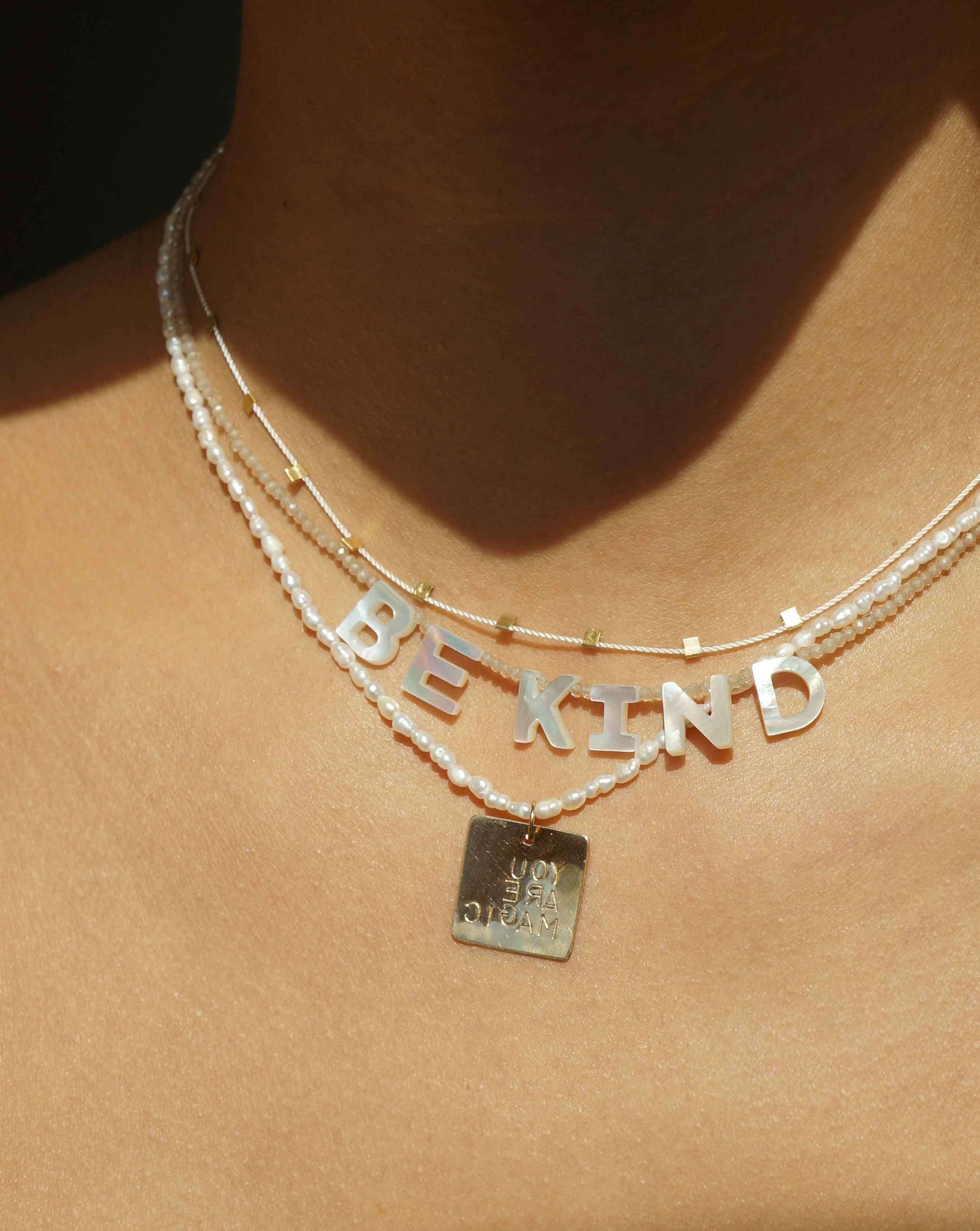 Kind Necklace by KOZAKH. A 16 to 18 inch adjustable length, faceted Zircon beads necklace, crafted with 14K Gold Filled, featuring hand carved Mother of Pearl letters spelling "BE KIND".