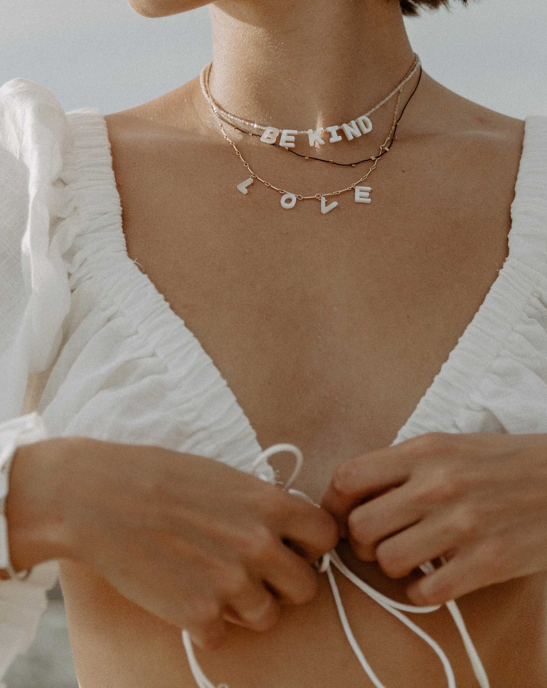 Kind Necklace by KOZAKH. A 16 to 18 inch adjustable length, faceted Zircon beads necklace, crafted with 14K Gold Filled, featuring hand carved Mother of Pearl letters spelling "BE KIND".