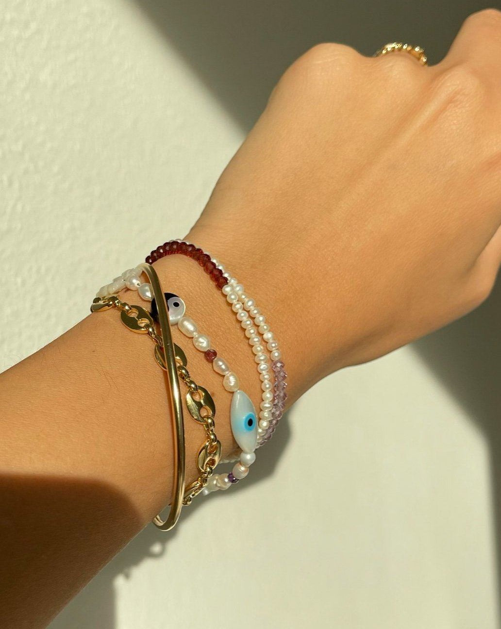 Lexie Bracelet by KOZAKH. A 6 to 7 inch adjustable length bracelet in 14K Gold Filled, featuring Pink Tourmaline slice, Mother of Pearl butterfly charm, round cut Malachite gemstone, Mother of Pearl eye charm, and 2.5mm to 3mm Fresh water pearls.