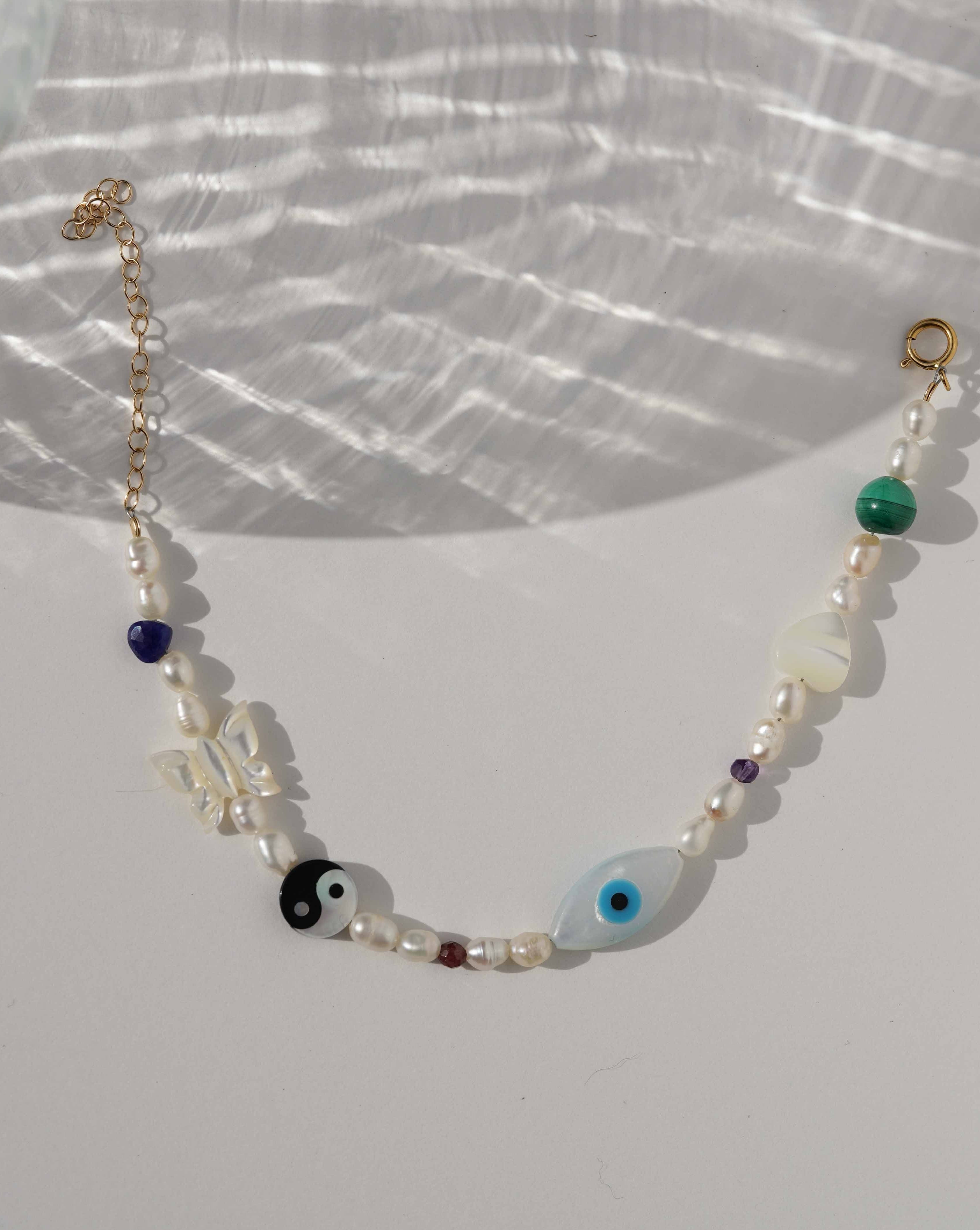 Lexie Bracelet by KOZAKH. A 6 to 7 inch adjustable length bracelet in 14K Gold Filled, featuring Pink Tourmaline slice, Mother of Pearl butterfly charm, round cut Malachite gemstone, Mother of Pearl eye charm, and 2.5mm to 3mm Fresh water pearls.