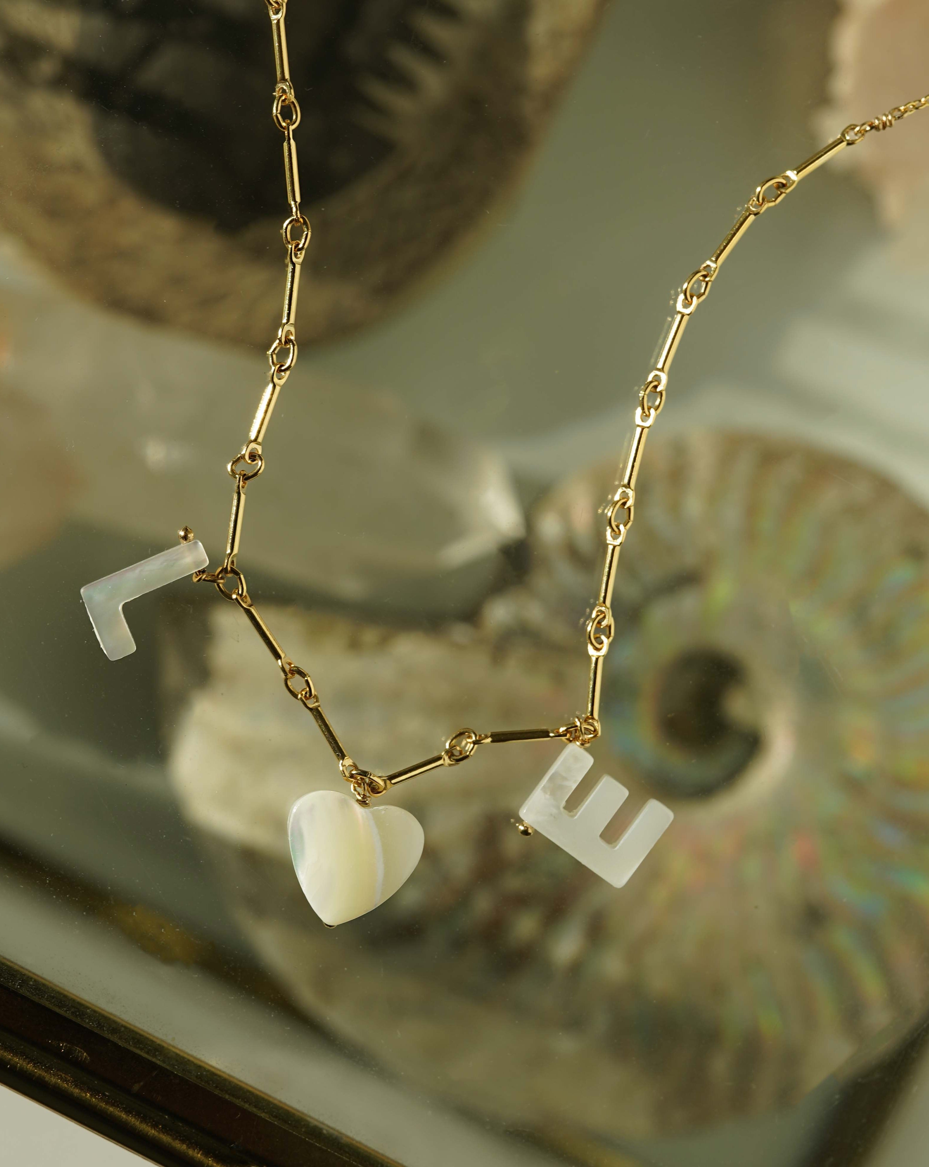 Love Necklace by KOZAKH. A 16 to 18 inch adjustable length necklace with linked bar chain on bottom half and flat link chain on top half, crafted in 14K Gold Filled, featuring a customizable word made from hand carved Mother of Pearl letters.