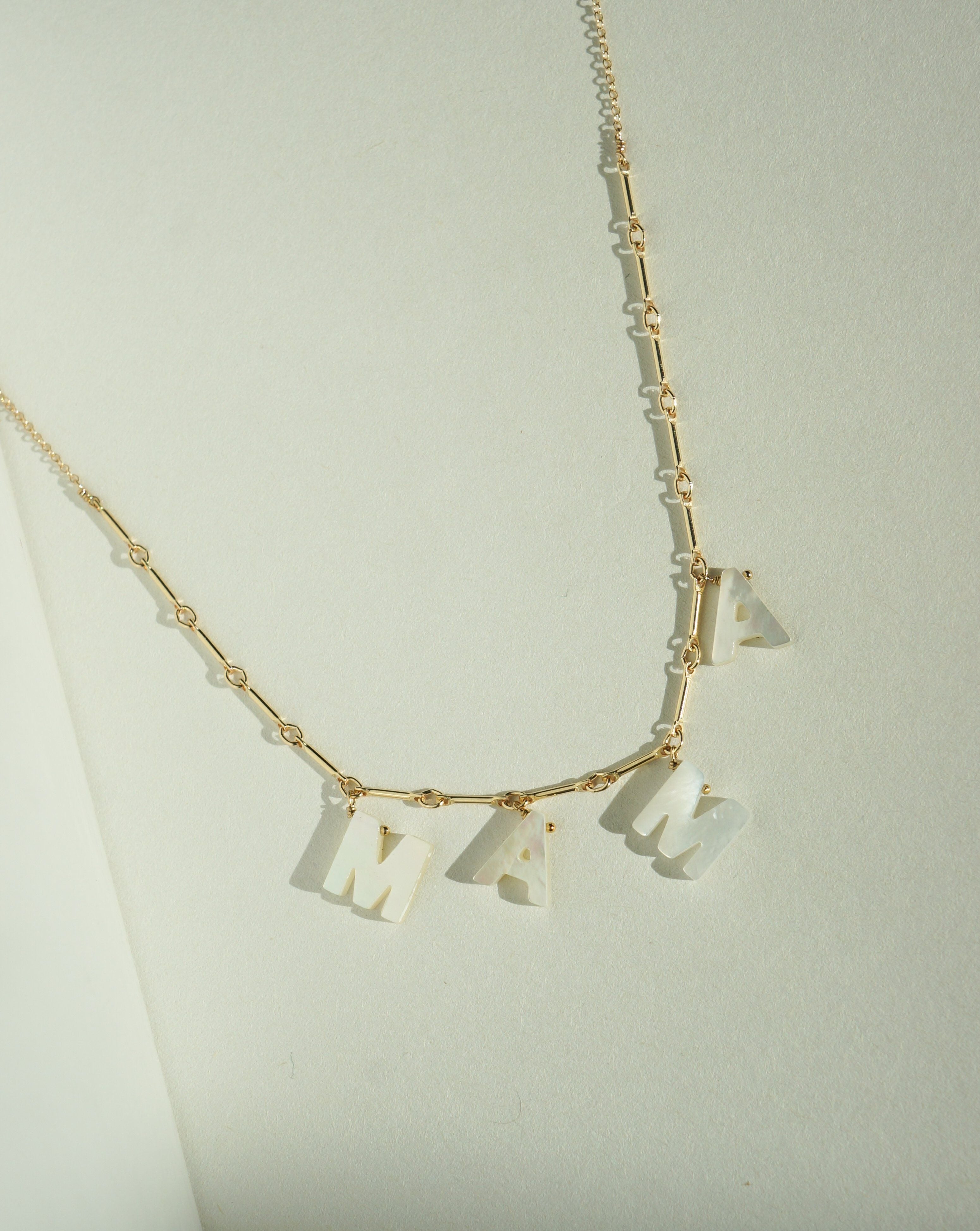 Love Necklace by KOZAKH. A 16 to 18 inch adjustable length necklace with linked bar chain on bottom half and flat link chain on top half, crafted in 14K Gold Filled, featuring a customizable word made from hand carved Mother of Pearl letters.