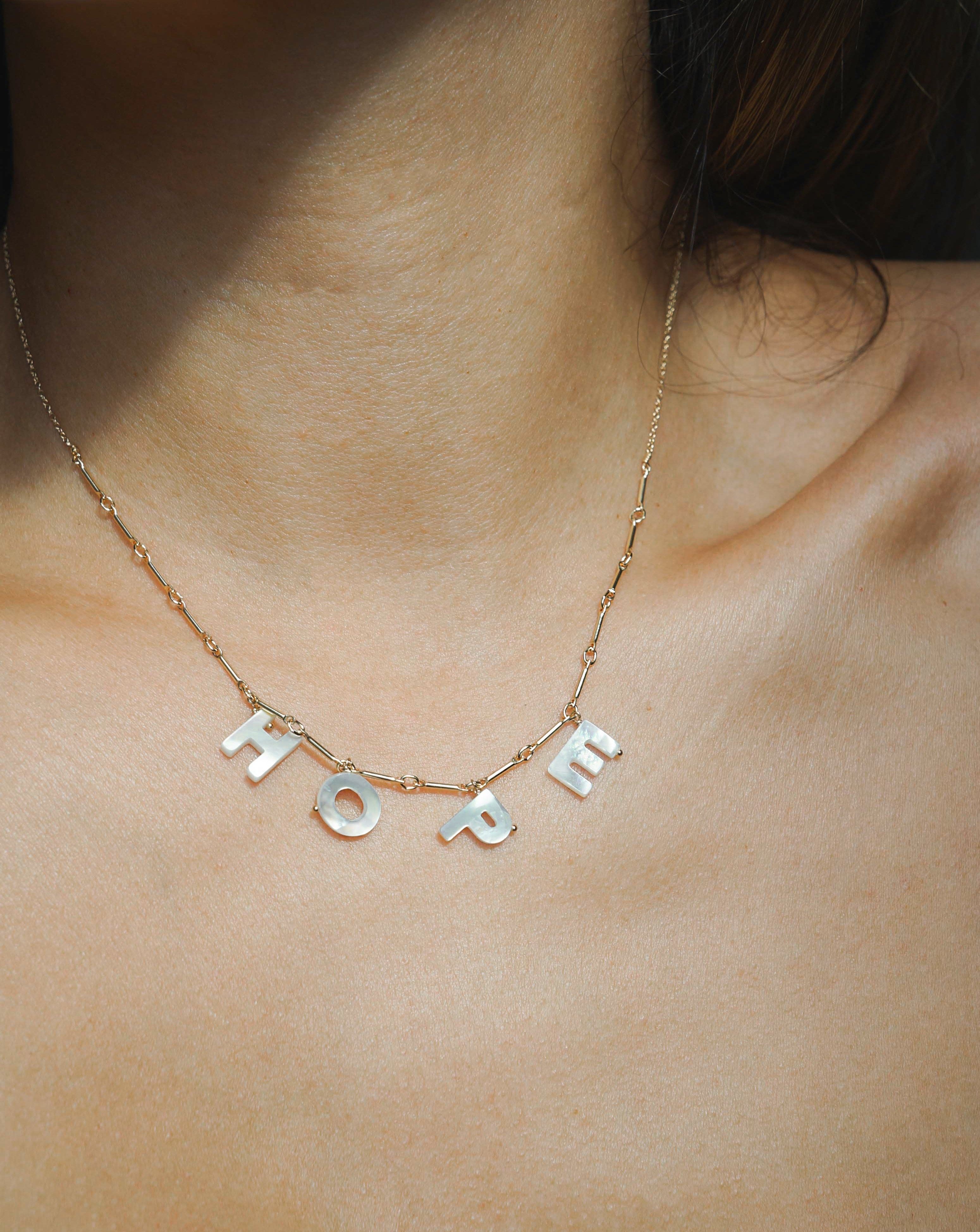 Love Necklace by KOZAKH. A 16 to 18 inch adjustable length necklace with linked bar chain on bottom half and flat link chain on top half, crafted in 14K Gold Filled, featuring a customizable word made from hand carved Mother of Pearl letters.