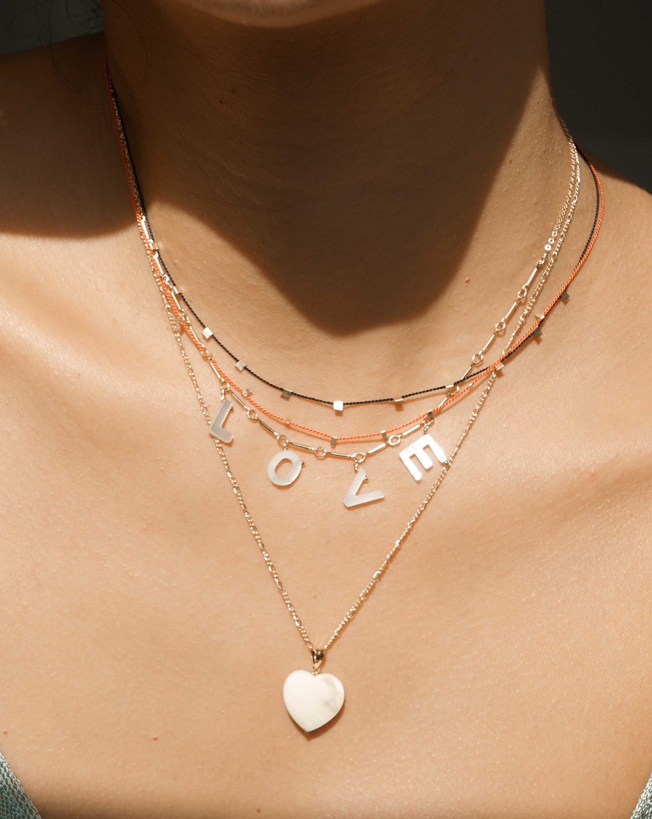 Love Necklace by KOZAKH. A 16 to 18 inch adjustable length necklace with linked bar chain on bottom half and flat link chain on top half, crafted in 14K Gold Filled, featuring a customizable word made from hand carved Mother of Pearl letters.