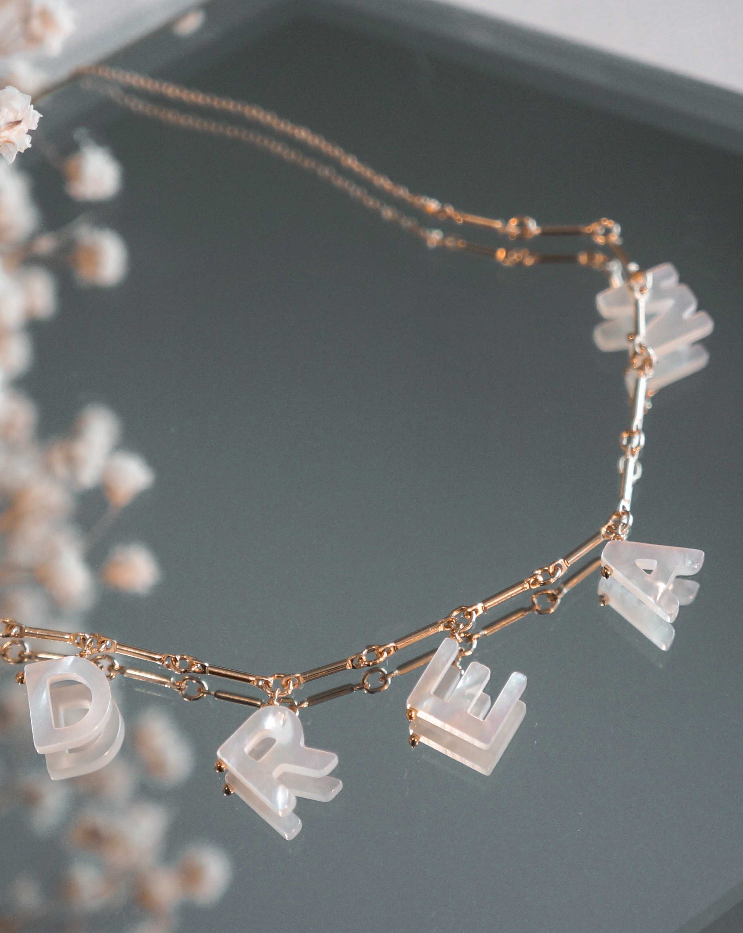 Love Necklace by KOZAKH. A 16 to 18 inch adjustable length necklace with linked bar chain on bottom half and flat link chain on top half, crafted in 14K Gold Filled, featuring a customizable word made from hand carved Mother of Pearl letters.