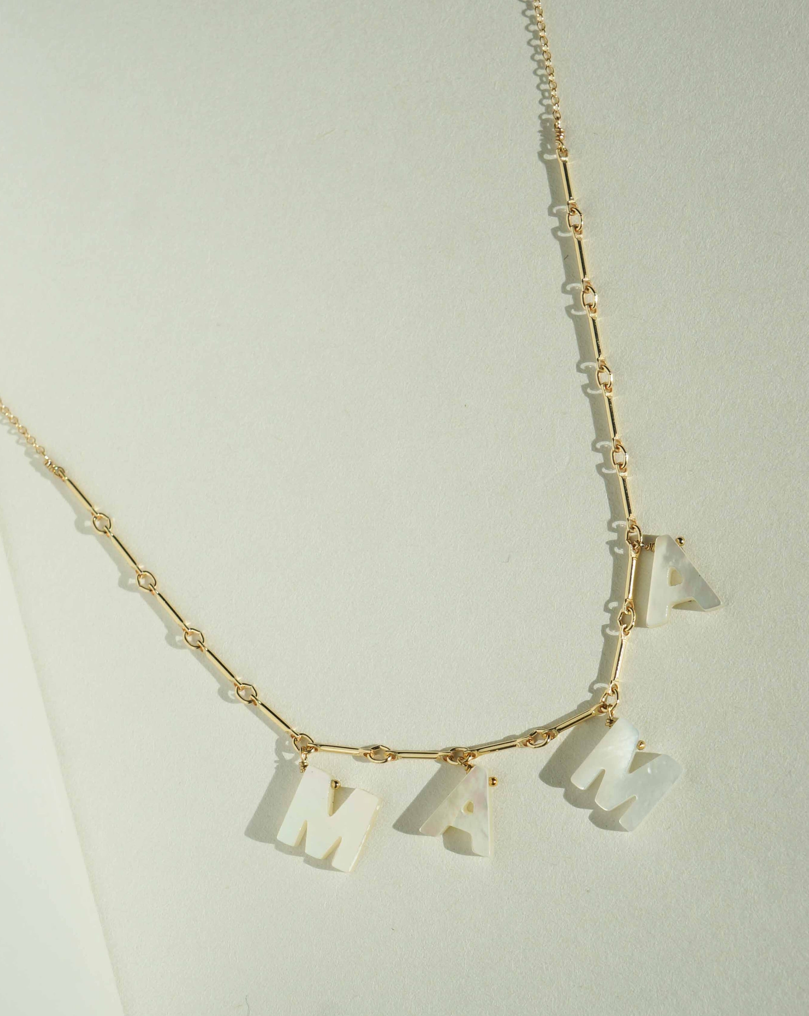 Mama Necklace by KOZAKH. A 16 to 18 inch adjustable length necklace with linked bar chain on bottom half and flat link chain on top half, crafted in 14K Gold Filled, featuring a customizable word made from hand carved Mother of Pearl letters.