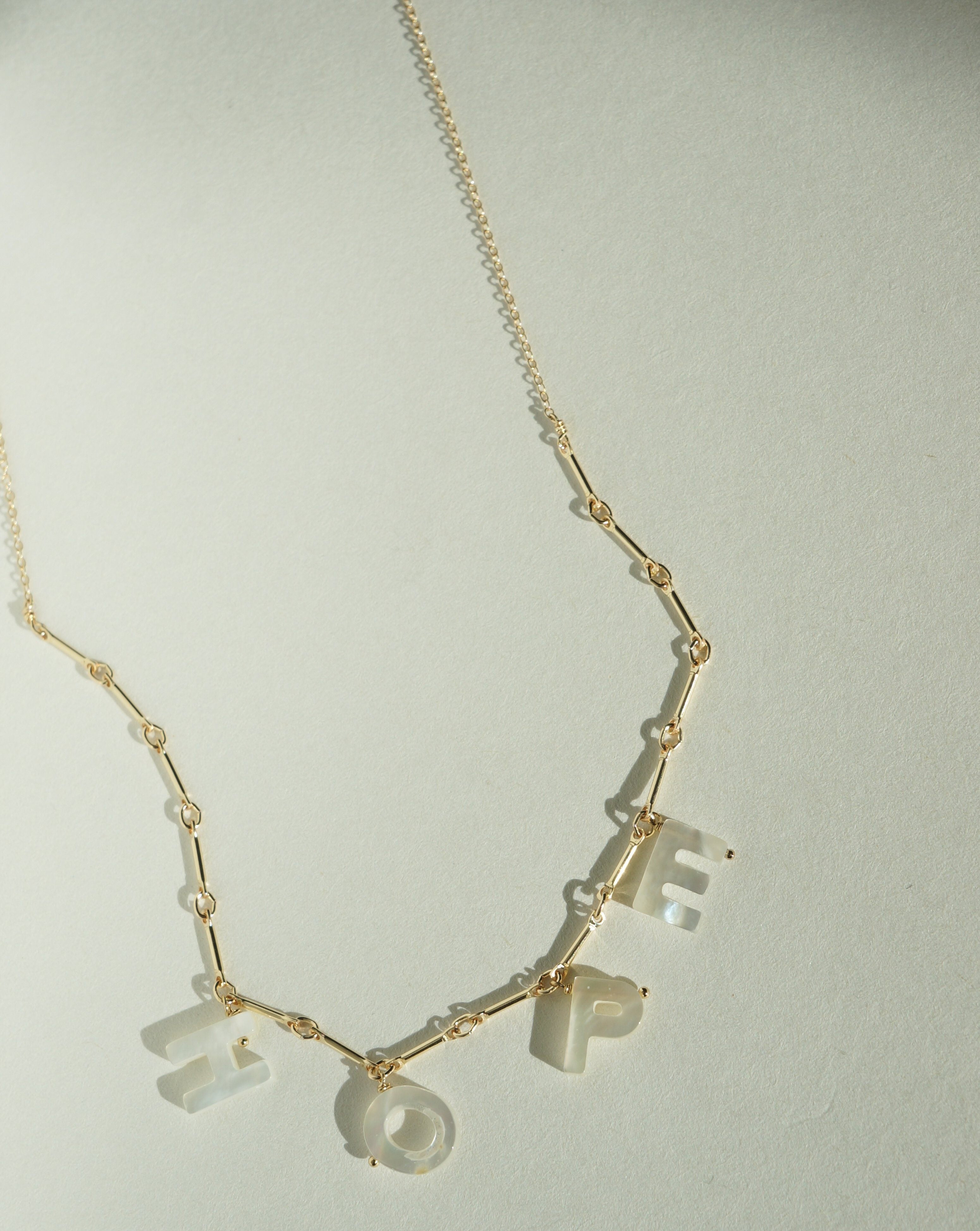 Mama Necklace by KOZAKH. A 16 to 18 inch adjustable length necklace with linked bar chain on bottom half and flat link chain on top half, crafted in 14K Gold Filled, featuring a customizable word made from hand carved Mother of Pearl letters.