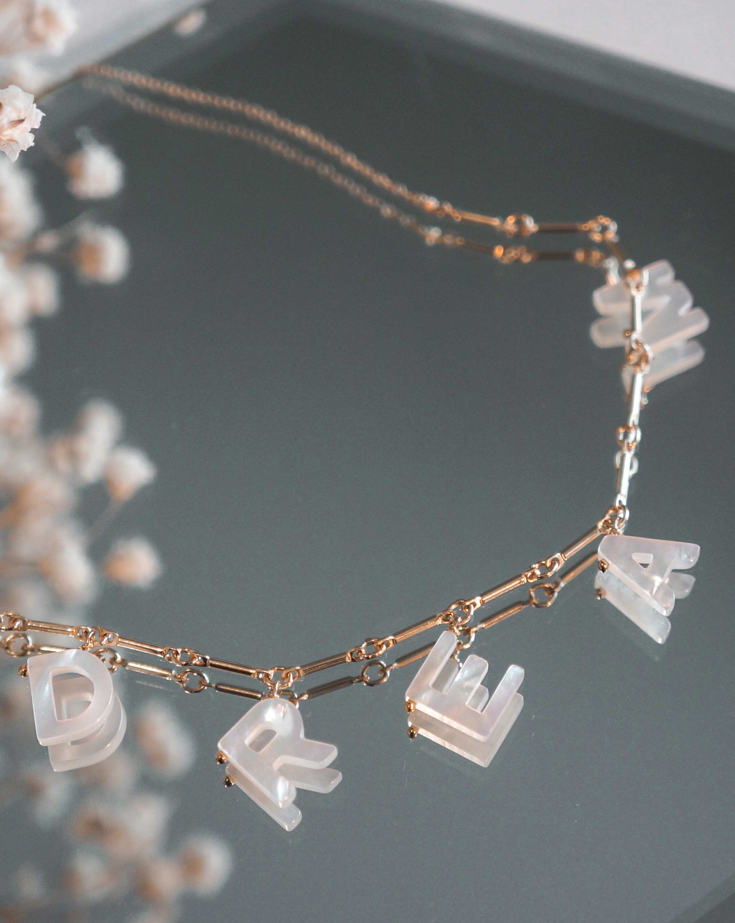 Mama Necklace by KOZAKH. A 16 to 18 inch adjustable length necklace with linked bar chain on bottom half and flat link chain on top half, crafted in 14K Gold Filled, featuring a customizable word made from hand carved Mother of Pearl letters.