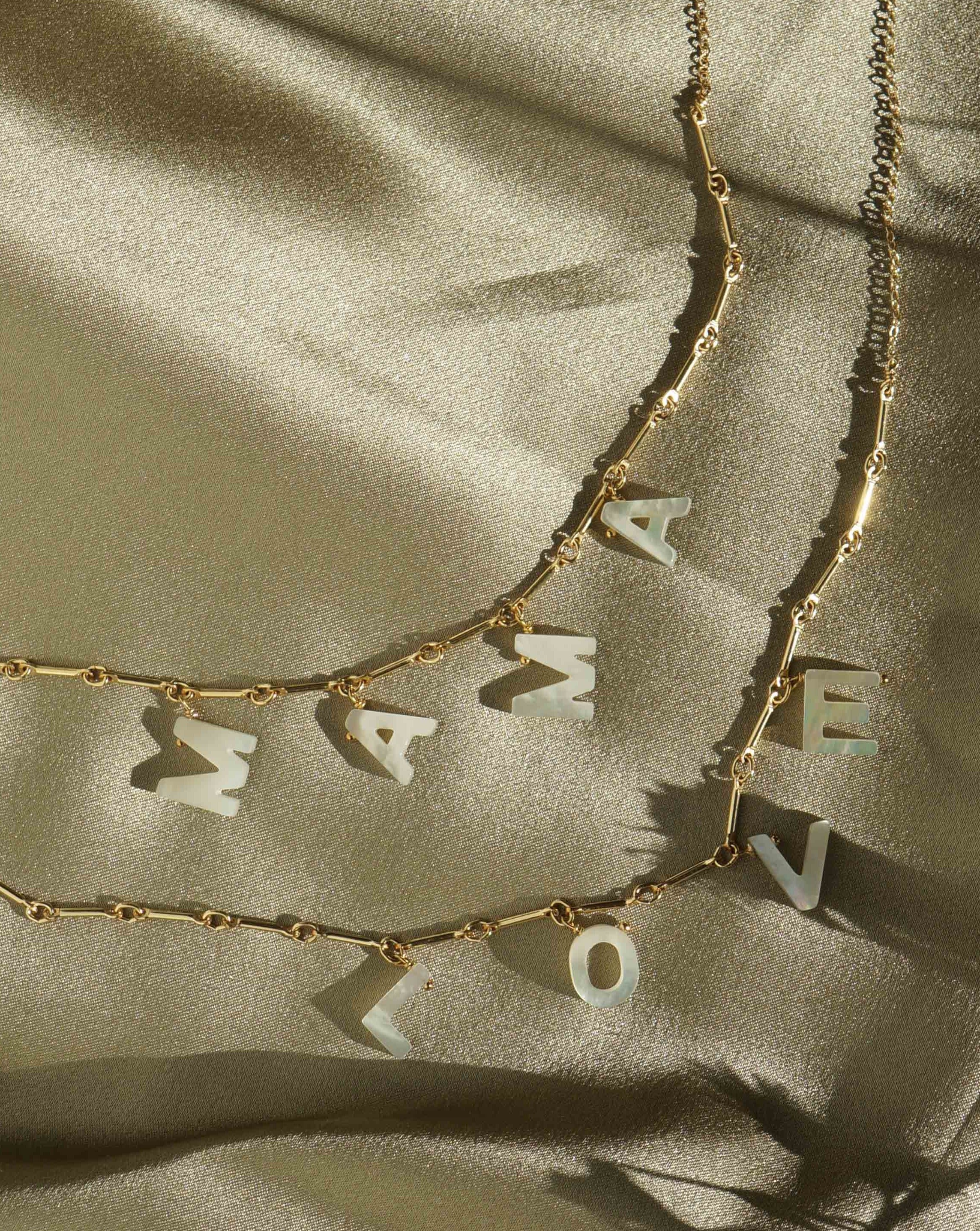Mama Necklace by KOZAKH. A 16 to 18 inch adjustable length necklace with linked bar chain on bottom half and flat link chain on top half, crafted in 14K Gold Filled, featuring a customizable word made from hand carved Mother of Pearl letters.