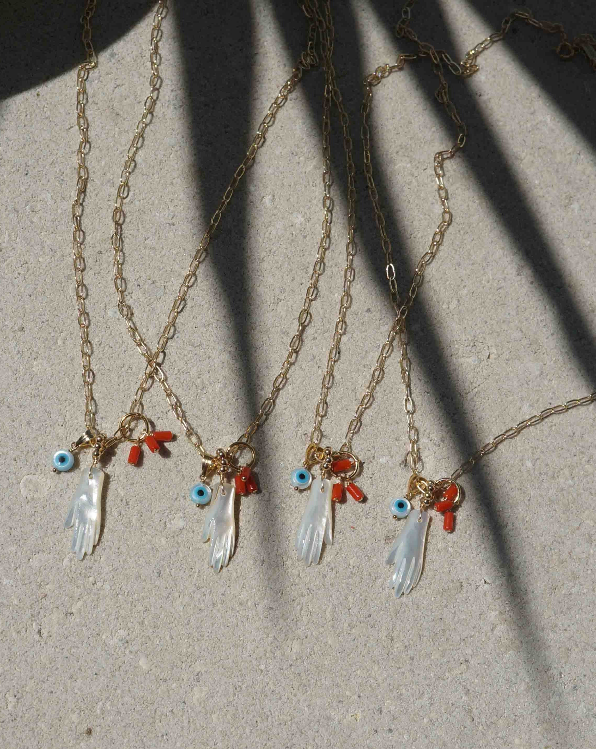 Manola Necklace by KOZAKH. An 18 to 20 inch adjustable length necklace in 14k Gold Filled, featuring a hand carved Mother of Pearl hand, a hand carved Mother of Pearl evil eye and a red coral bead.