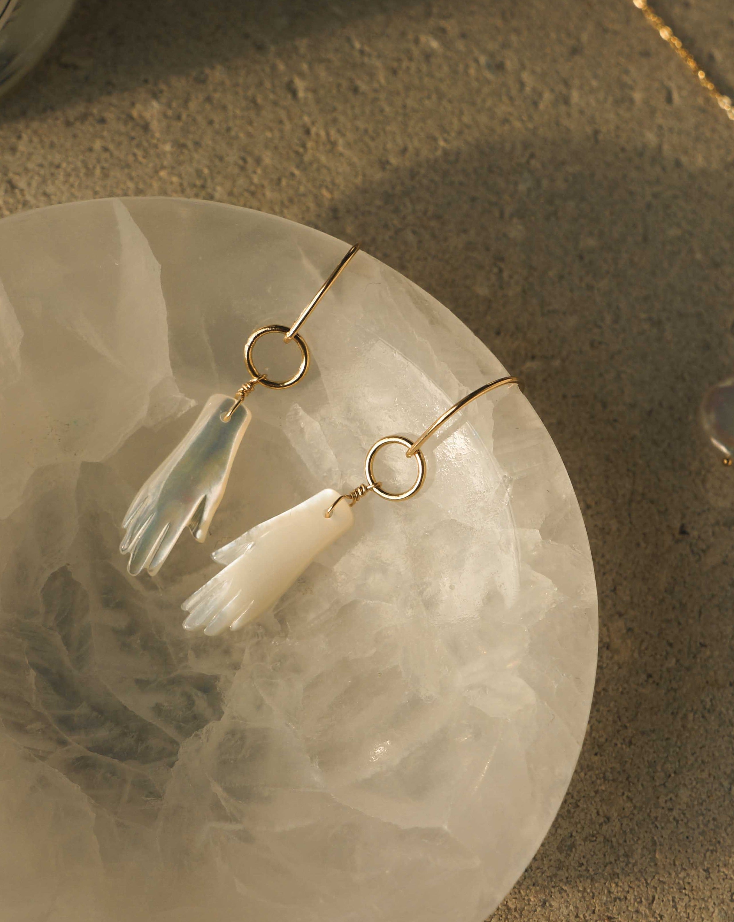 Manos Hoop Earrings by KOZAKH. Hook earrings crafted in 14K Gold Filled, featuring a hand carved Mother of Pearl hand.