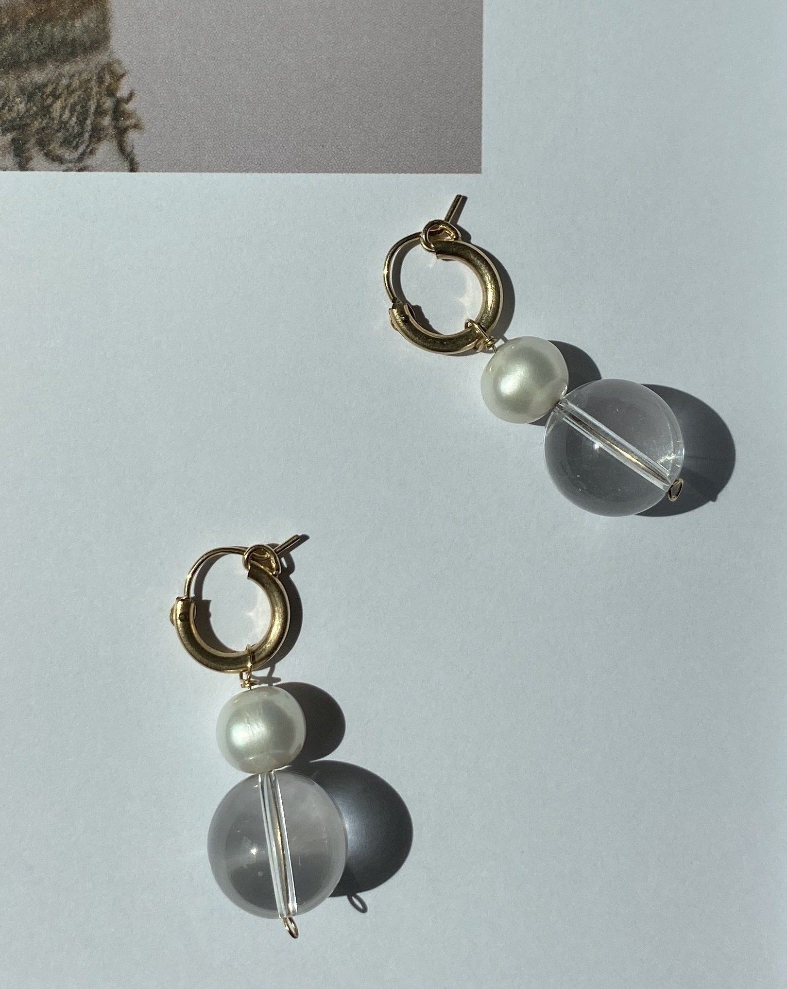 Milae Hoop Earrings by KOZAKH. 12mm snap closure hoop earrings, crafted in 14K Gold Filled, featuring a Crystal Quartz and an 8mm white Pearl.