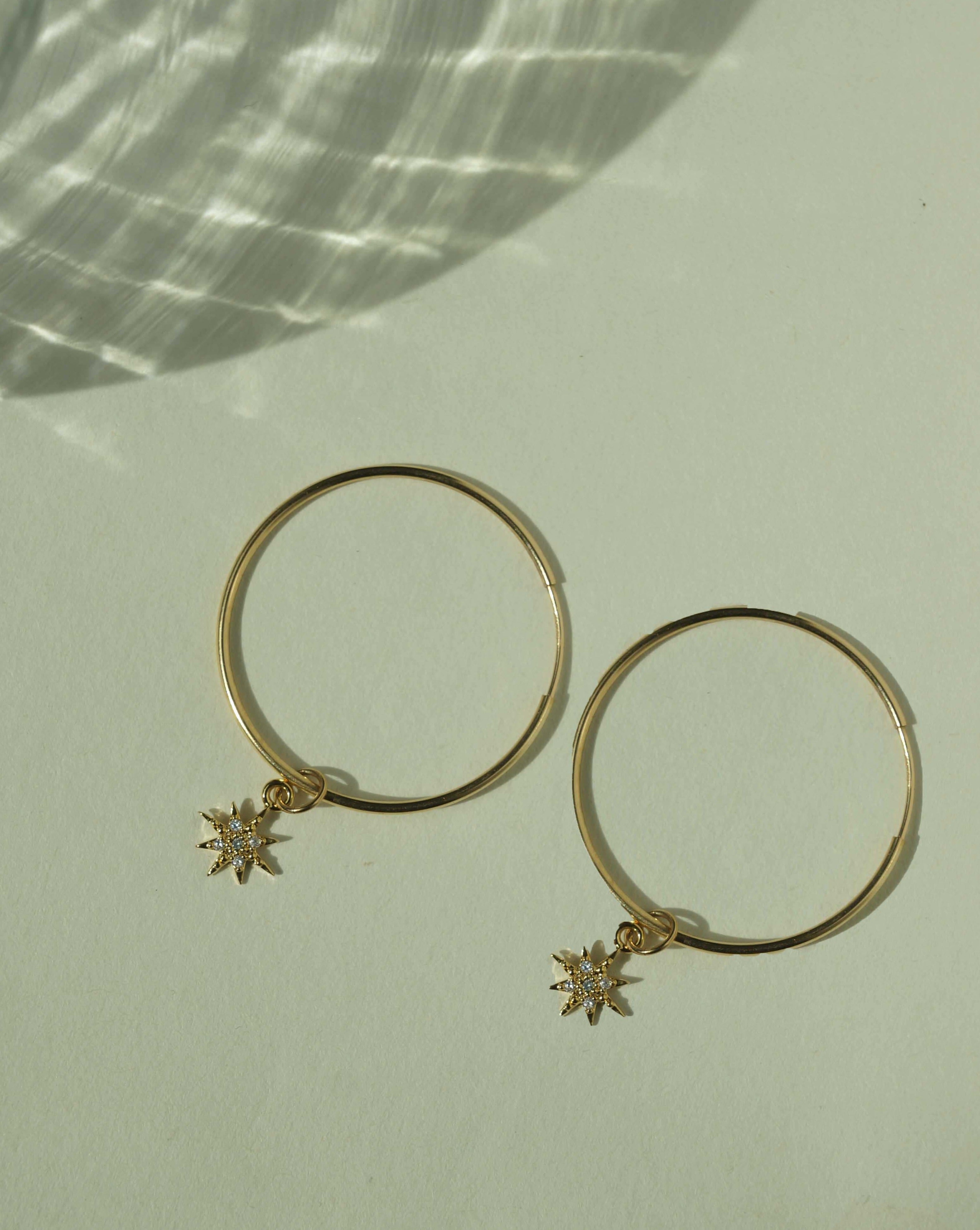Soleil Hoop Earrings by KOZAKH. 30mm hoop earrings, crafted in 14K Gold Filled, featuring a dangling Cubic Zirconia 6 point star charm.