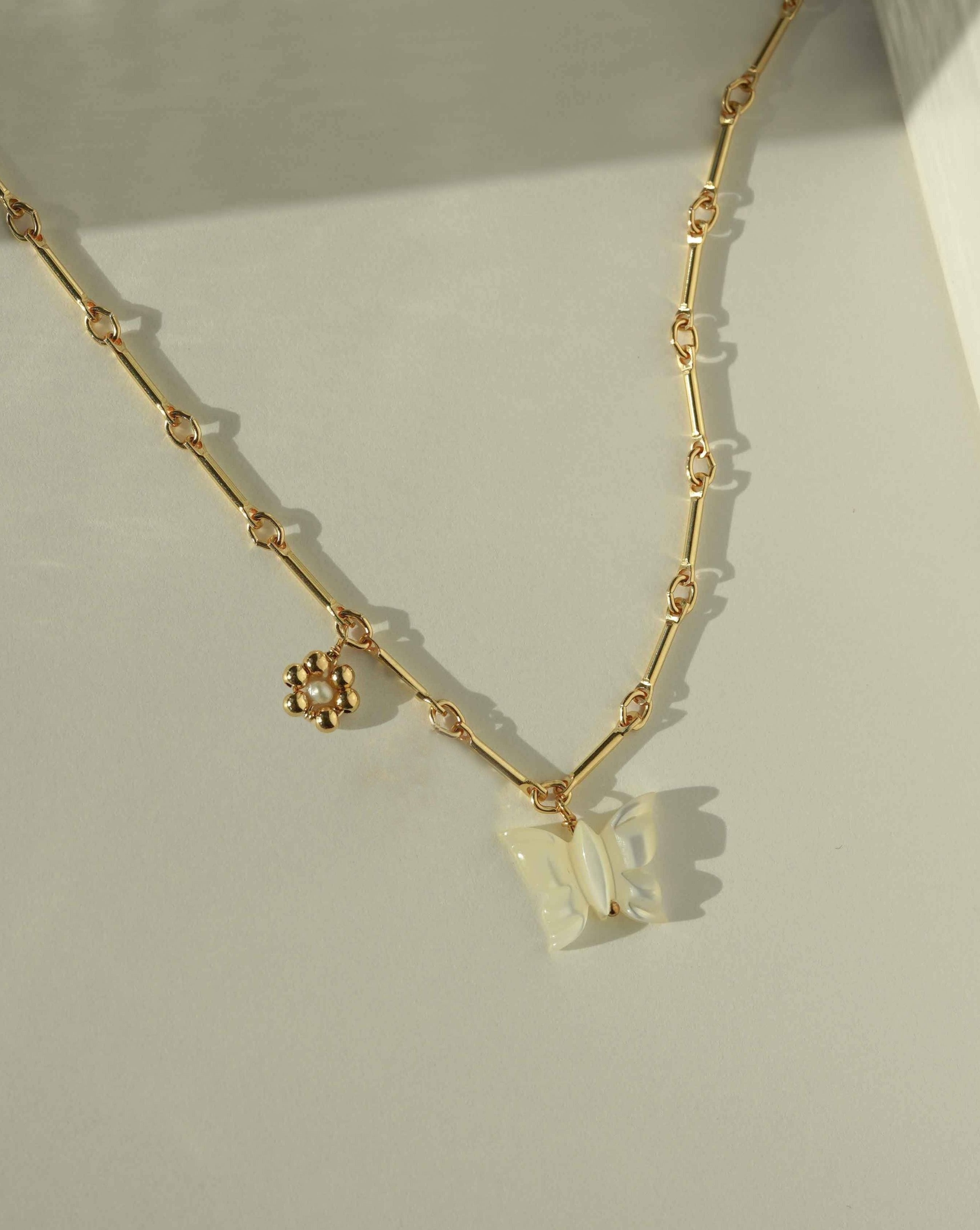 Tinley Necklace by KOZAKH. A 16 to 18 inch adjustable length necklace, with flat cable chain on top half and bar link chain on bottom half, crafted in 14K Gold Filled, featuring a hand-carved Mother of Pearl butterfly charm and a handmade gold beaded daisy with 2mm pearl in the center.