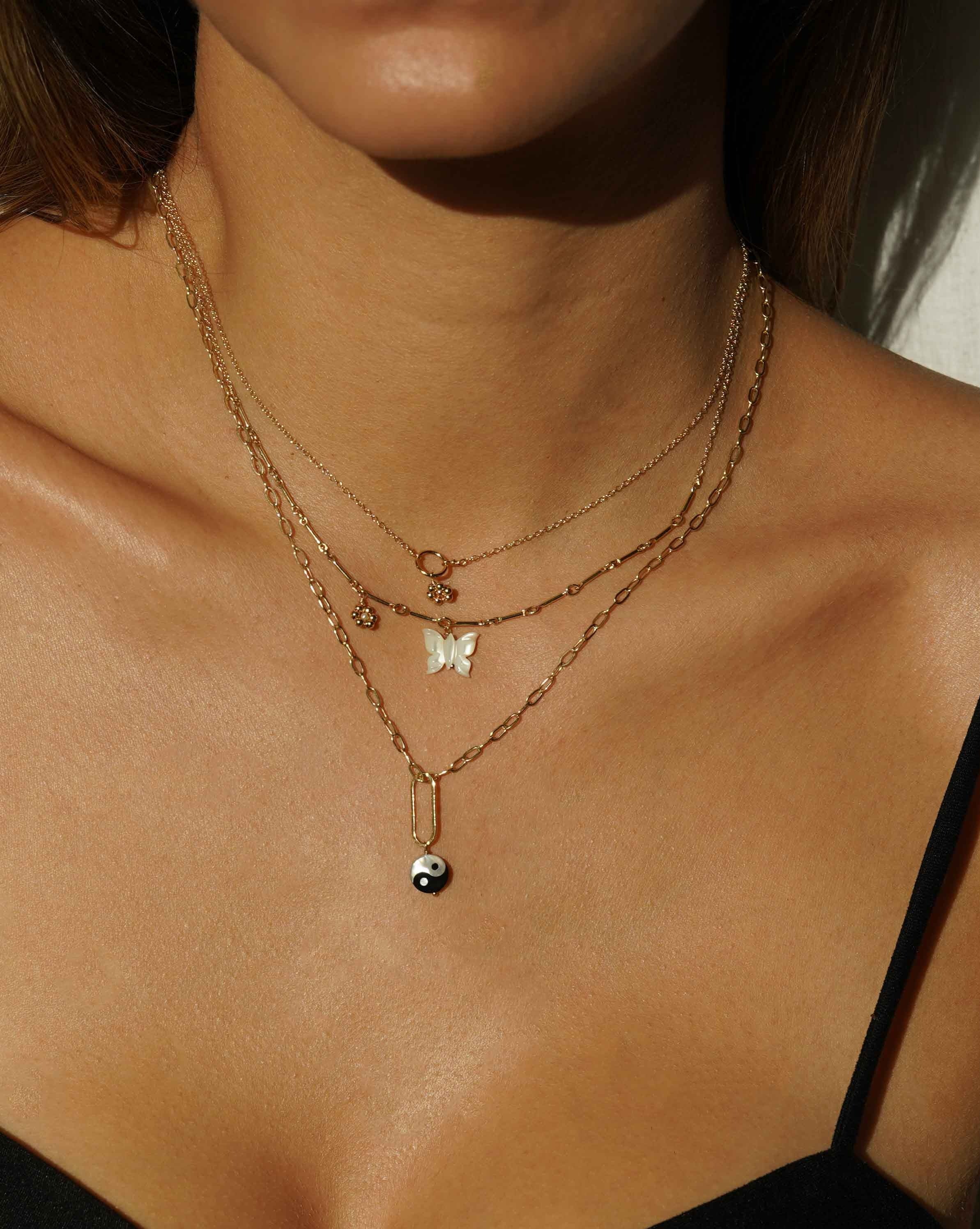 Tinley Necklace by KOZAKH. A 16 to 18 inch adjustable length necklace, with flat cable chain on top half and bar link chain on bottom half, crafted in 14K Gold Filled, featuring a hand-carved Mother of Pearl butterfly charm and a handmade gold beaded daisy with 2mm pearl in the center.