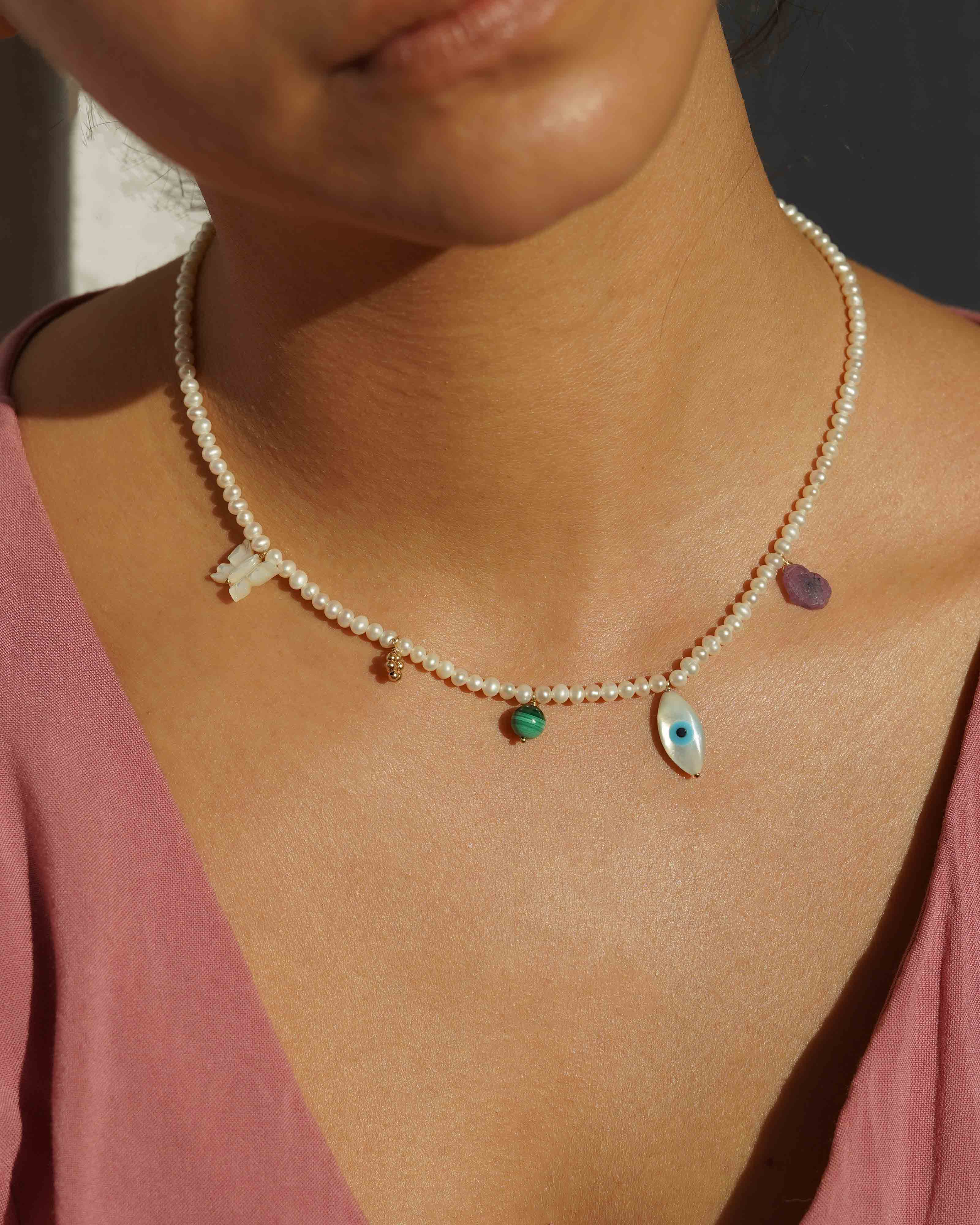 Valery Necklace by KOZAKH. A 16 to 18 inch adjustable length necklace, with 16 inch strand of 3mm Freshwater Pearls, clasp crafted in 14K Gold Filled, featuring Pink Tourmaline slice, Mother of Pearl butterfly charm, smooth round Malachite gemstone, Mother of Pearl eye charm, and handmade gold beaded daisy charm.