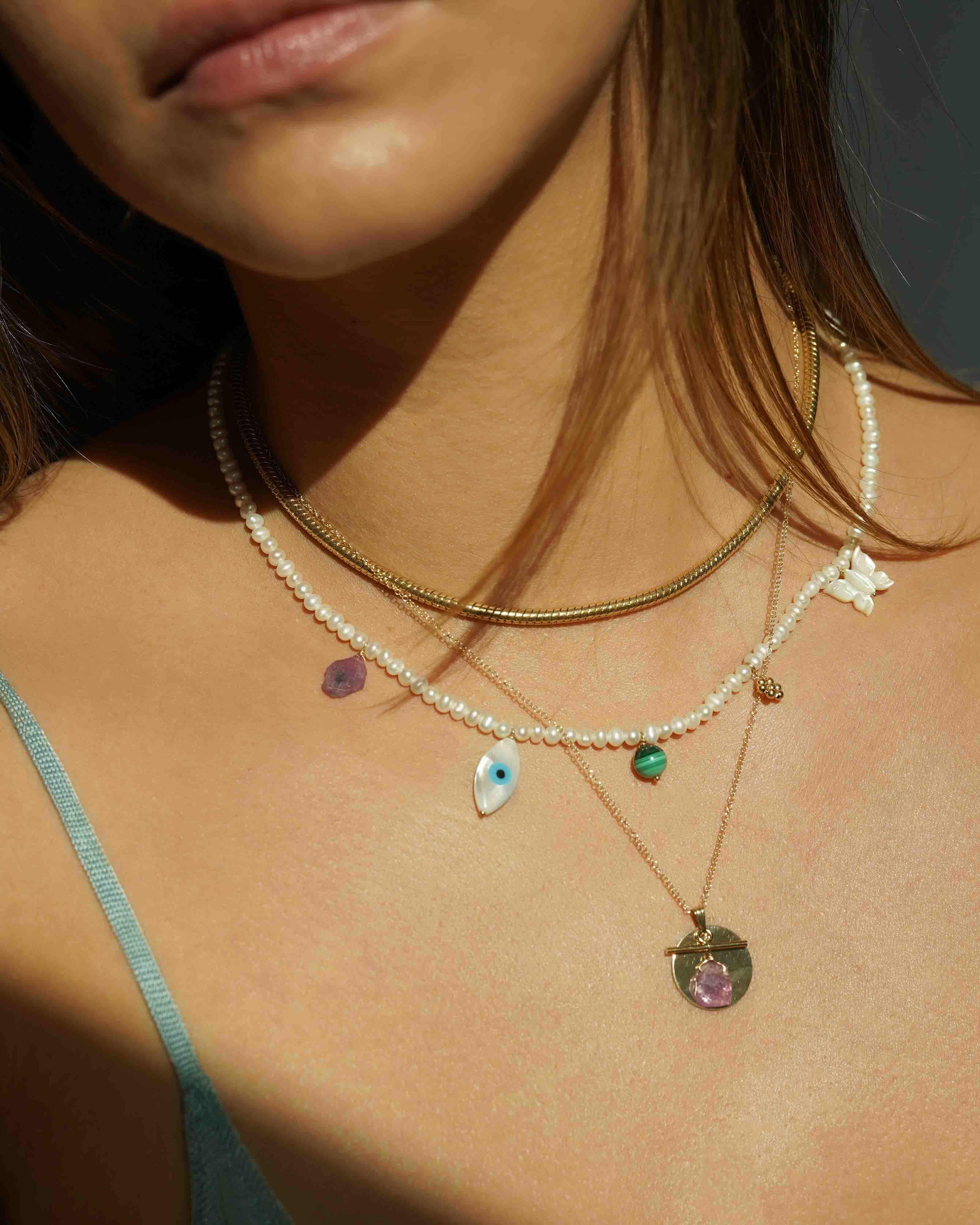 Valery Necklace by KOZAKH. A 16 to 18 inch adjustable length necklace, with 16 inch strand of 3mm Freshwater Pearls, clasp crafted in 14K Gold Filled, featuring Pink Tourmaline slice, Mother of Pearl butterfly charm, smooth round Malachite gemstone, Mother of Pearl eye charm, and handmade gold beaded daisy charm.