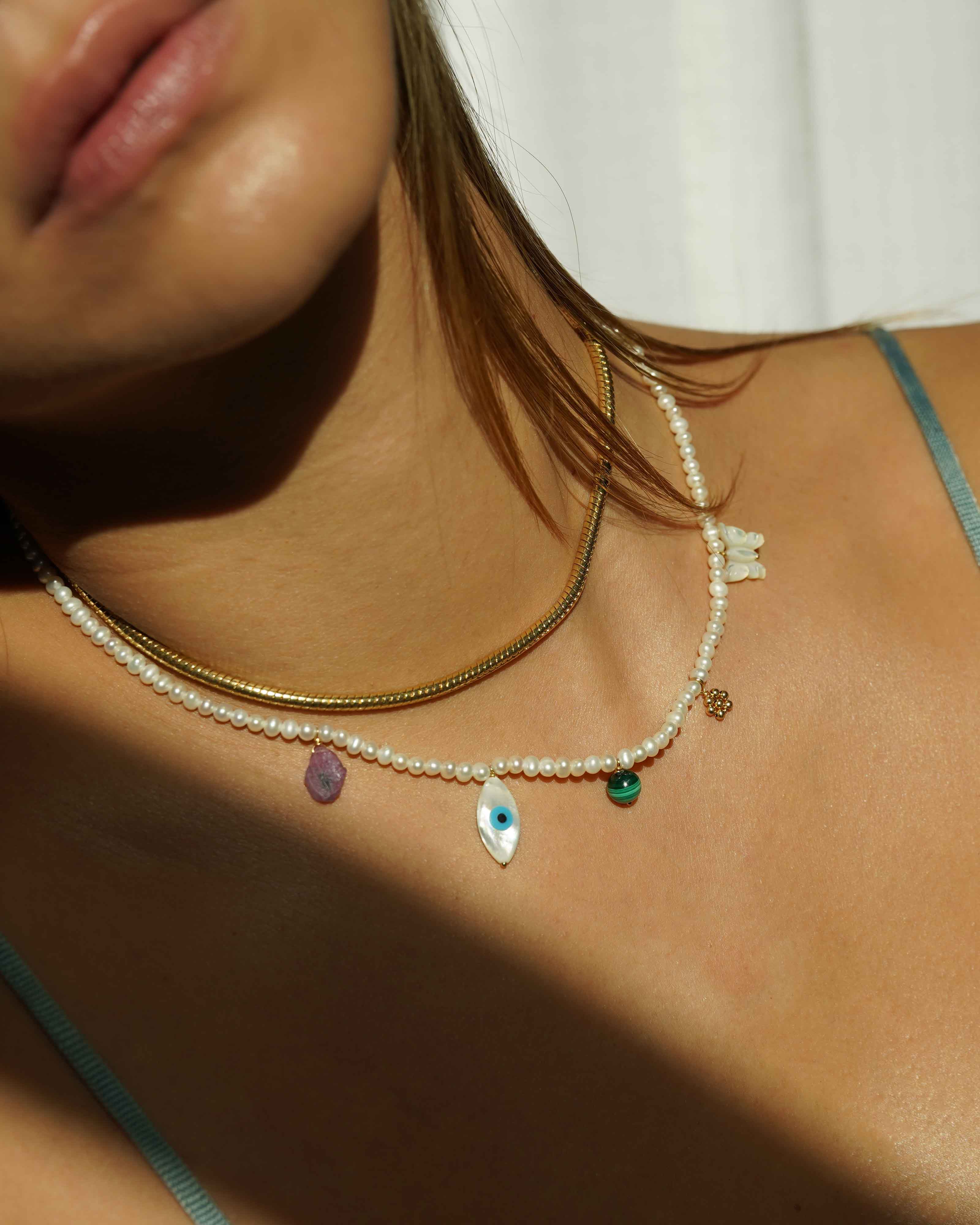 Valery Necklace by KOZAKH. A 16 to 18 inch adjustable length necklace, with 16 inch strand of 3mm Freshwater Pearls, clasp crafted in 14K Gold Filled, featuring Pink Tourmaline slice, Mother of Pearl butterfly charm, smooth round Malachite gemstone, Mother of Pearl eye charm, and handmade gold beaded daisy charm.