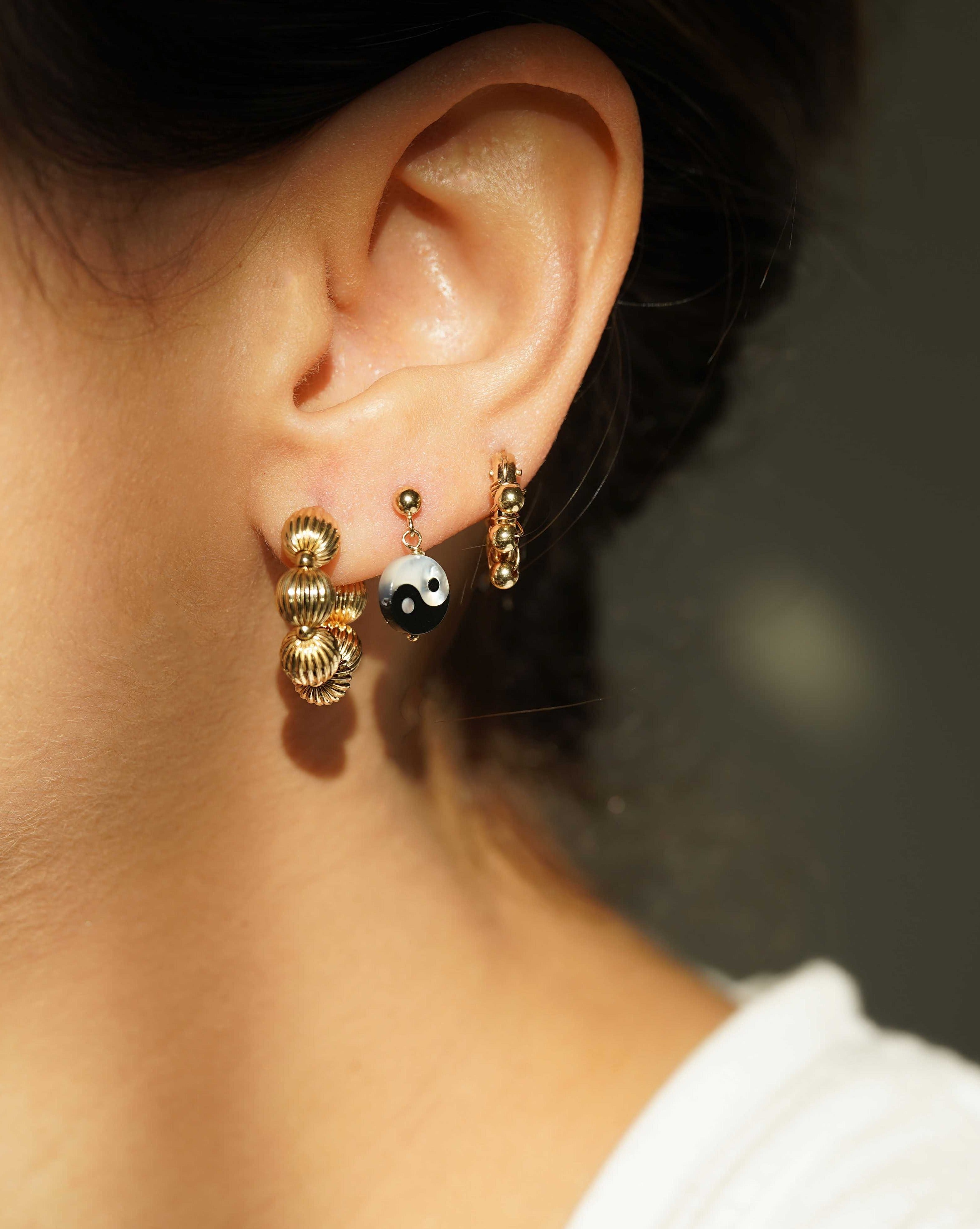 Yin Yang Earrings by KOZAKH. 3mm Ball stud earrings with 0.5 inch drop length, crafted in 14K Gold Filled, featuring a hand carved Mother of Pearl Yin Yang charm.