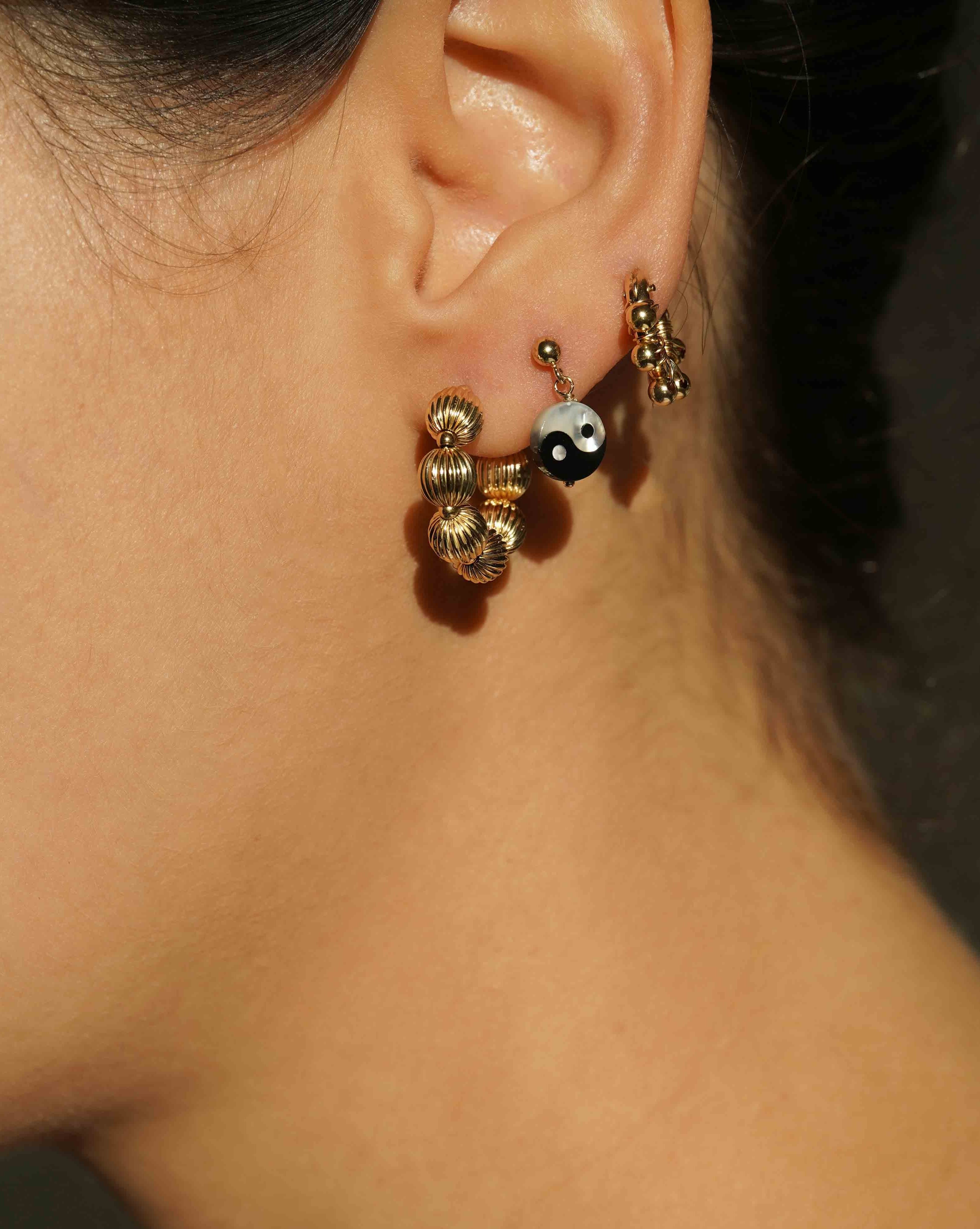 Yin Yang Earrings by KOZAKH. 3mm Ball stud earrings with 0.5 inch drop length, crafted in 14K Gold Filled, featuring a hand carved Mother of Pearl Yin Yang charm.