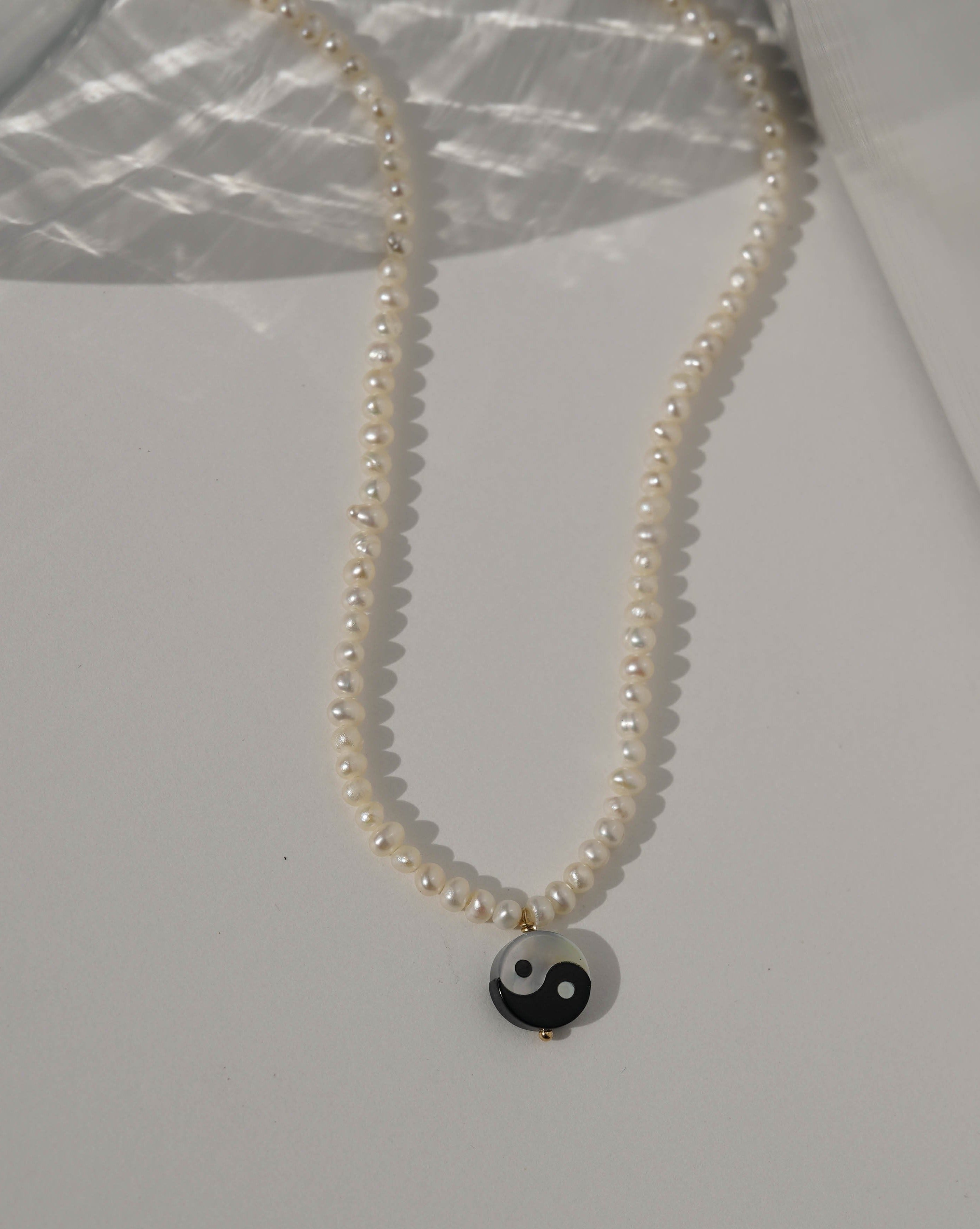 Yin Yang Pearl Necklace by KOZAKH. A 16 to 18 inch adjustable length necklace, with 16 inch strand of 3.5mm Freshwater Pearls, clasp crafted in 14K Gold Filled, featuring a hand carved Mother of pearl Yin Yang charm.