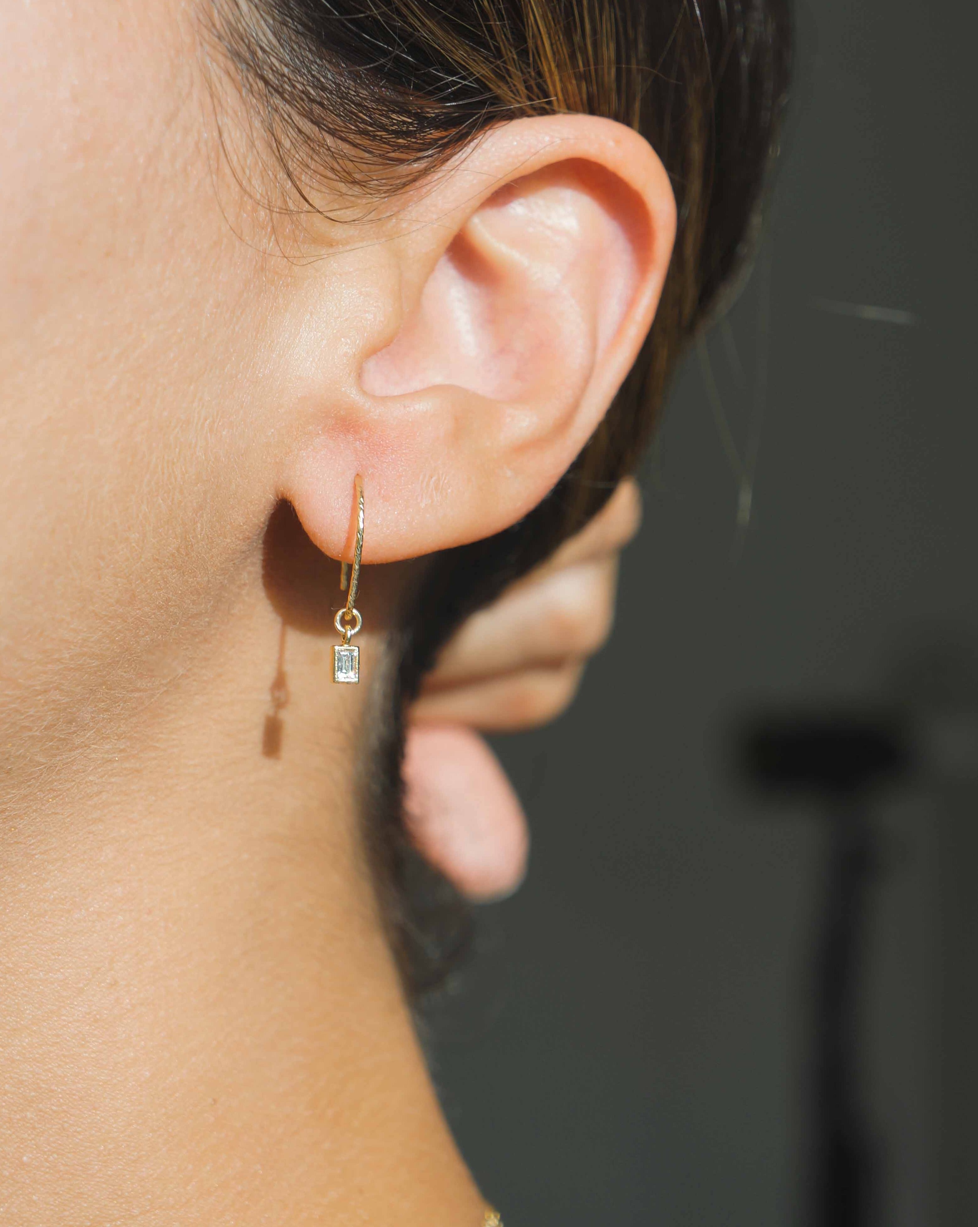 You Cadre Earrings by KOZAKH. Diamond textured hook earrings, crafted in 14K Gold Filled, featuring a CUbic Zirconia charm.