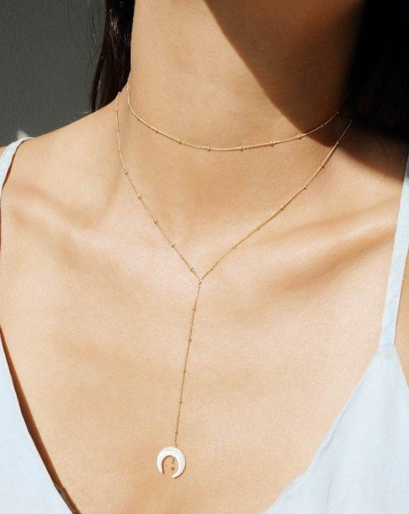Baque Lar Necklace by KOZAKH. A 16 to 18 inch adjustable length, 3 inches chain drop lariat style necklace in 14K Gold Filled, featuring a hand-carved Mother of Pearl moon charm and a 2mm Swarovski Crystal.