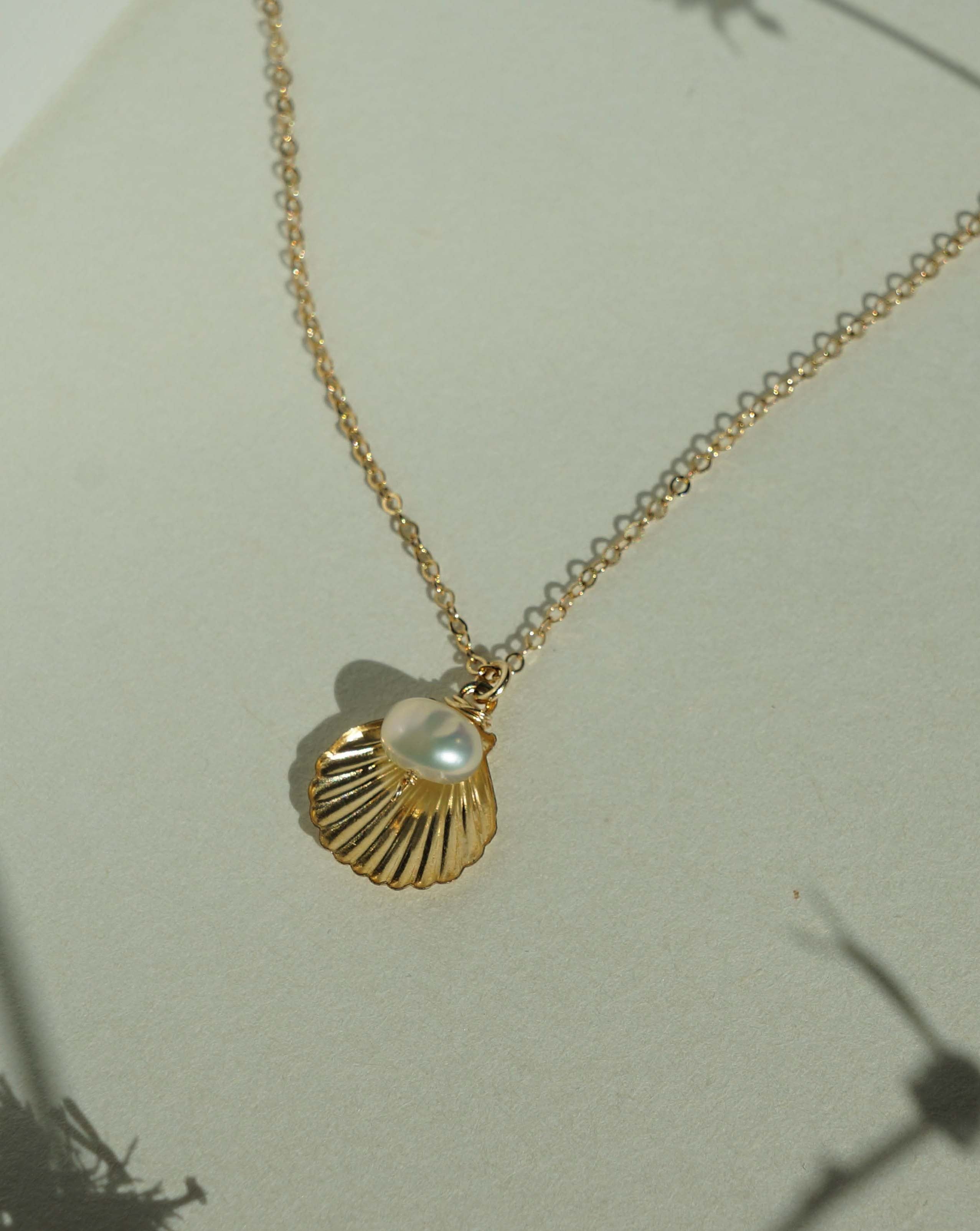 Belle Necklace by KOZAKH. A 16 to 18 inch adjustable length necklace in 14K Gold Filled, featuring a 5mm flat irregular Pearl and a Shell charm.