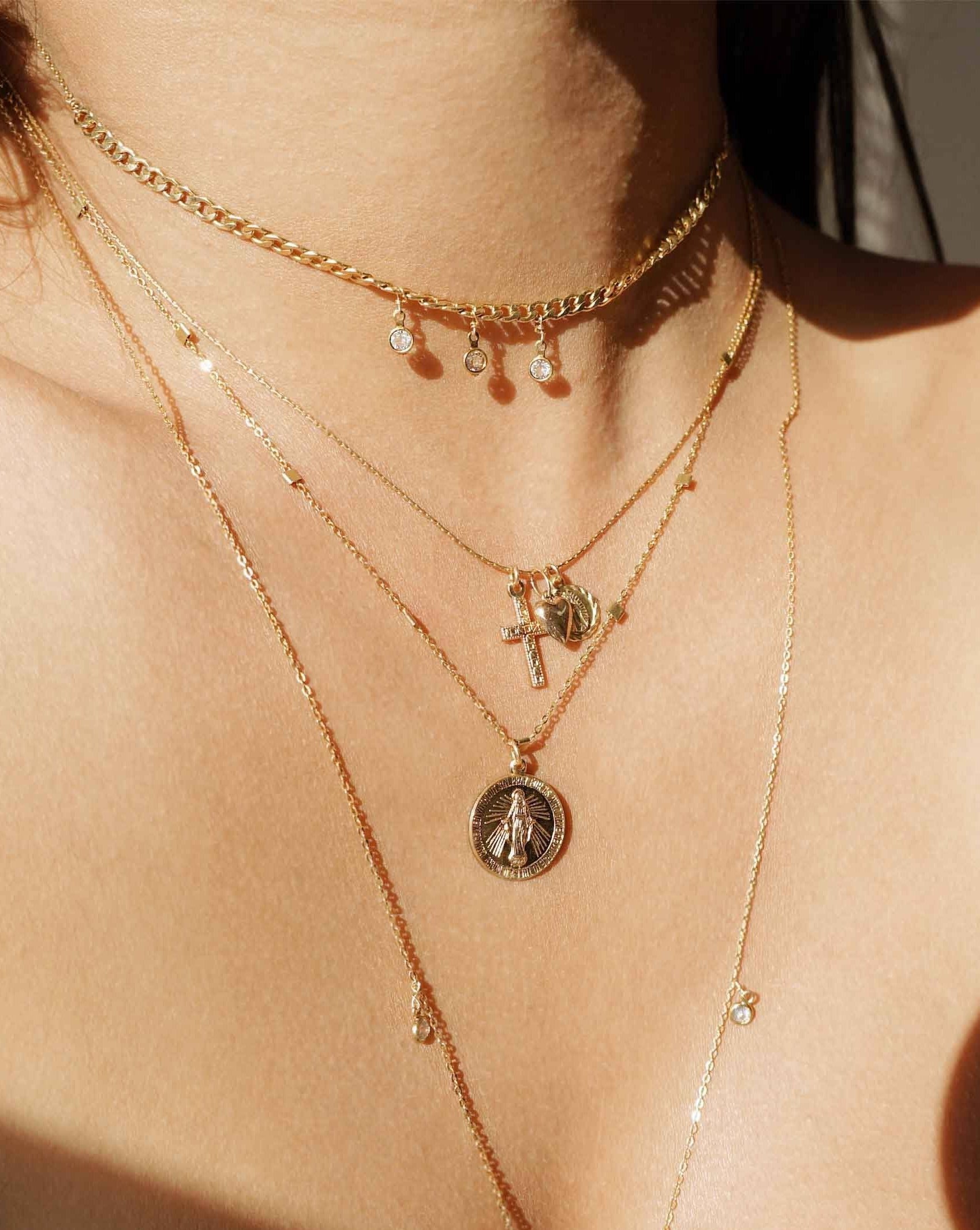 Domingo Necklace by KOZAKH. A 16 to 18 inch adjustable length necklace in 14K Gold Filled, featuring a Saint Christopher medallion, a 6mm Heart charm, and a Filigree decorated cross.