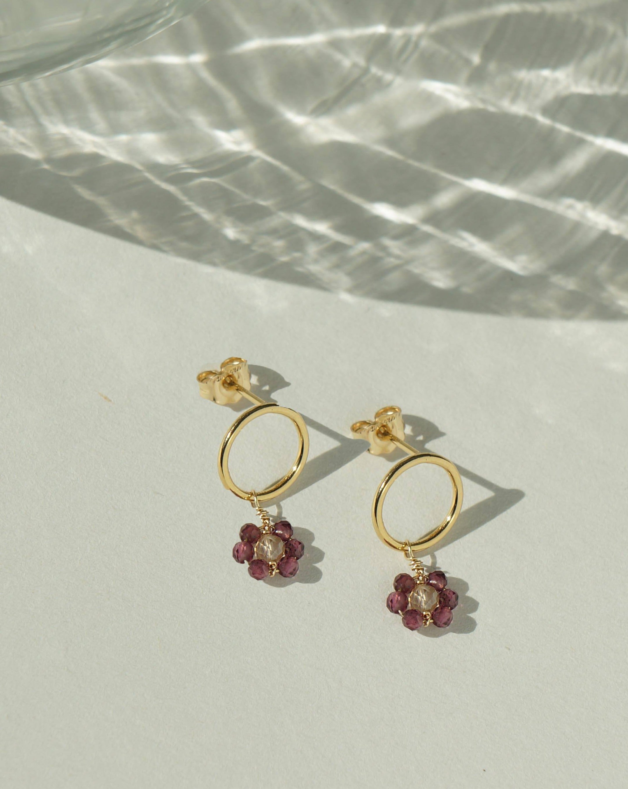 Florcitas Earrings by KOZAKH. 10mm circle studs, crafted in 14K Gold Filled, featuring 2mm Garnet gems and 3mm Imperial Topaz forming a daisy.