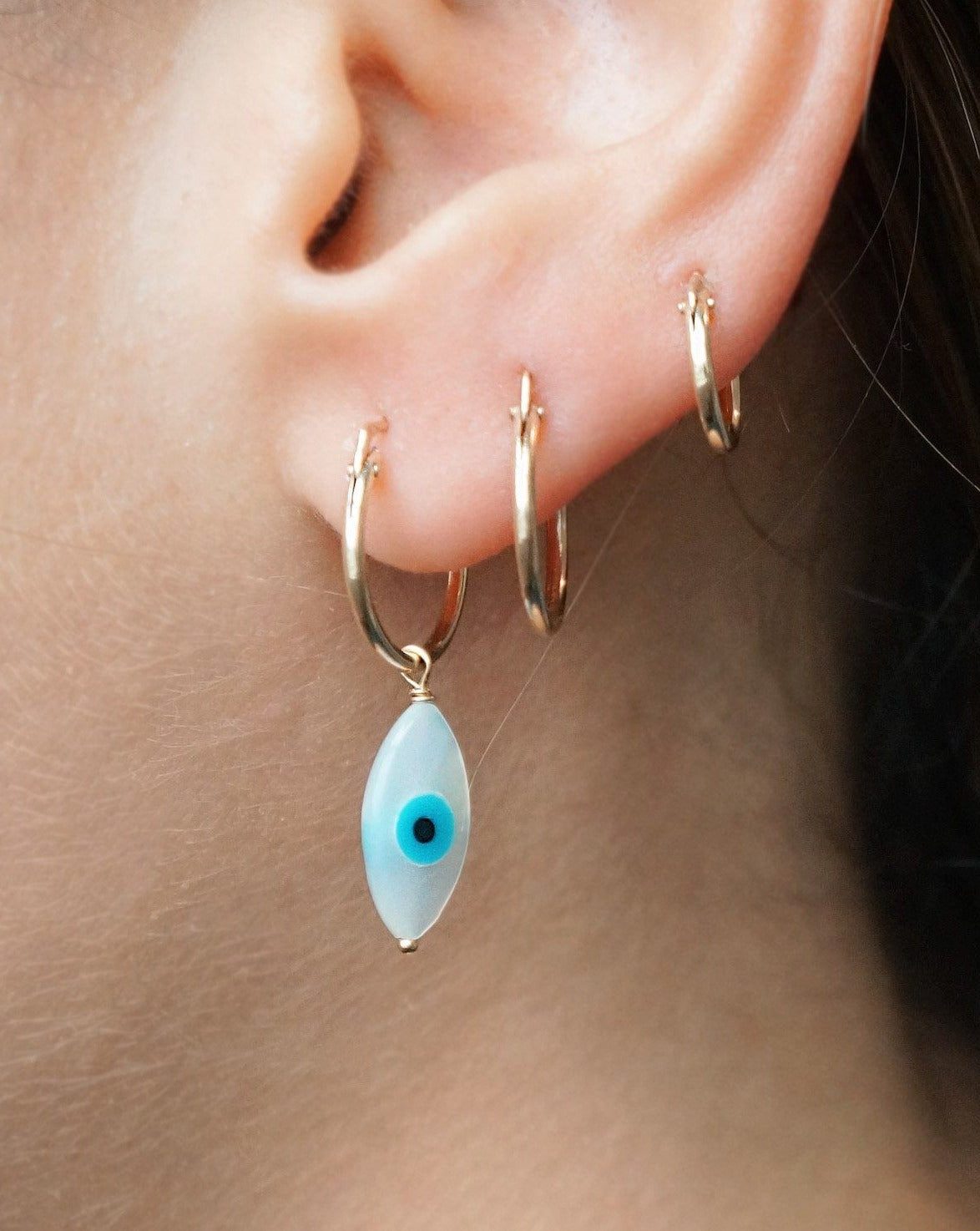 Ima Hoop Earrings by KOZAKH. 15mm snap closure hoop earrings, crafted in 14K Gold Filled, featuring hand carved Mother of Pearl Evil Eye charm.