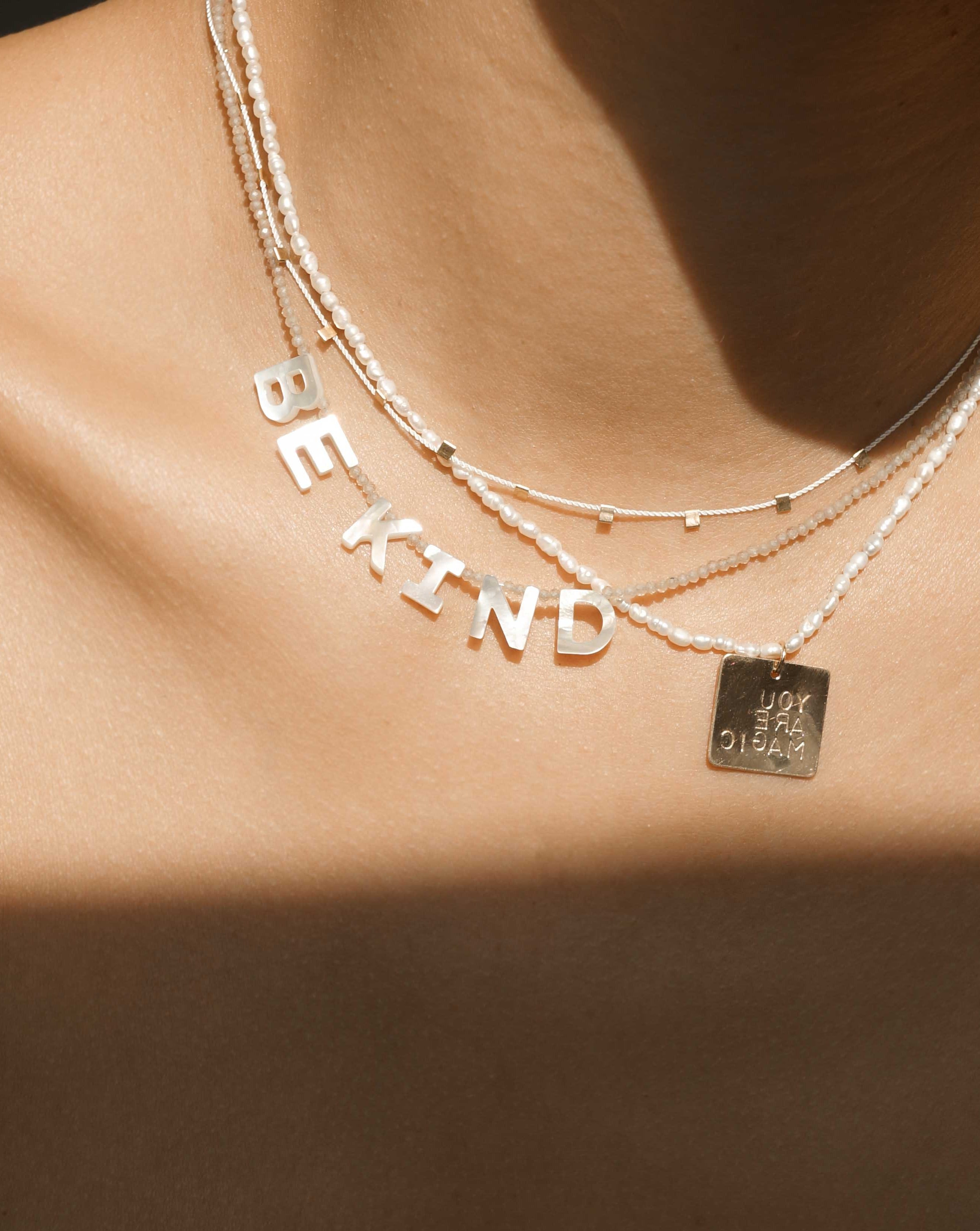 Kind Necklace by KOZAKH. A 16 to 18 inch adjustable length, faceted Zircon beads necklace, crafted with 14K Gold Filled, featuring hand carved Mother of Pearl letters spelling "BE KIND".