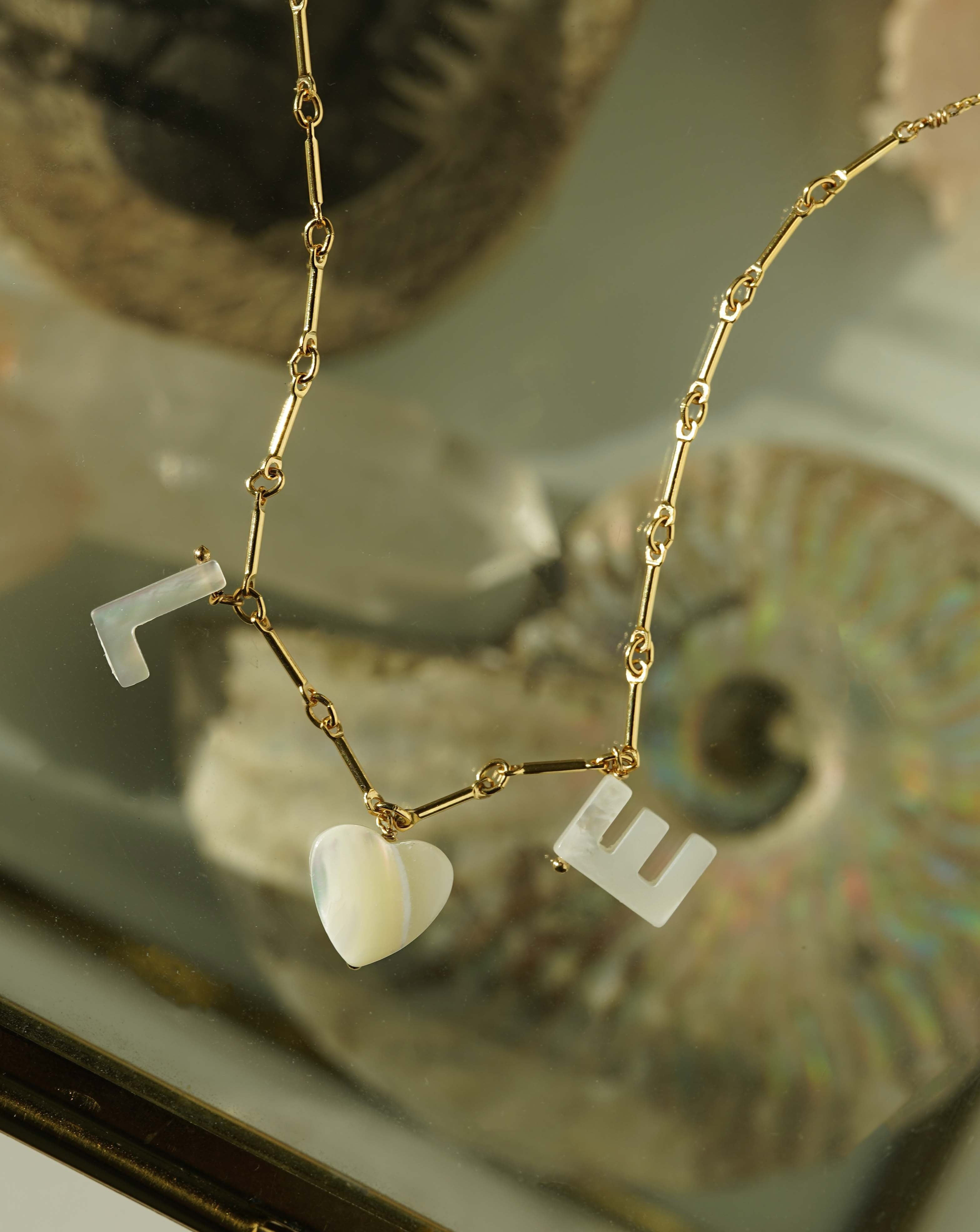 Mama Necklace by KOZAKH. A 16 to 18 inch adjustable length necklace with linked bar chain on bottom half and flat link chain on top half, crafted in 14K Gold Filled, featuring a customizable word made from hand carved Mother of Pearl letters.