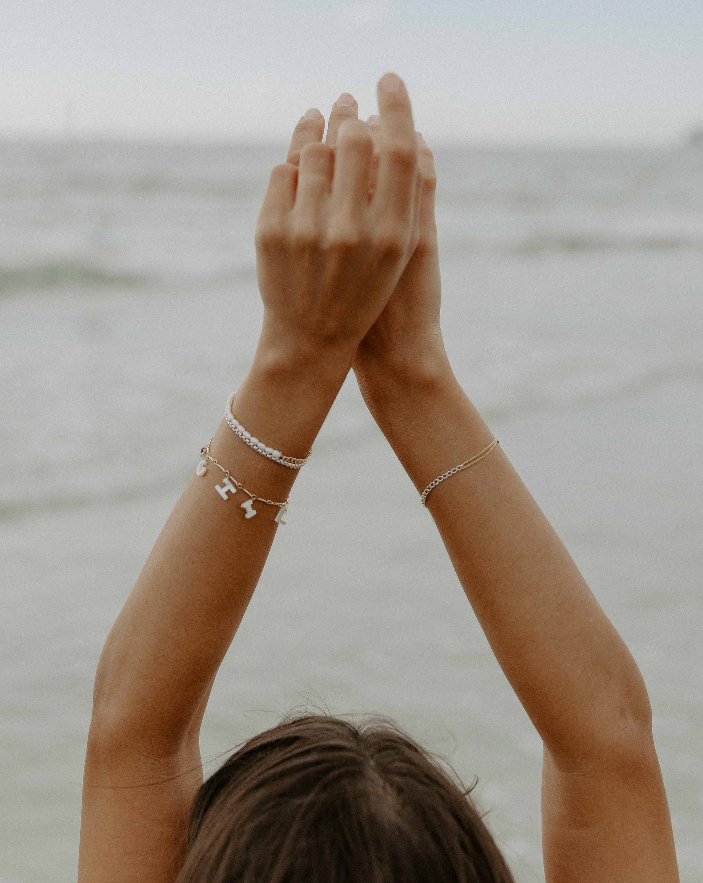 Shore Bracelet by KOZAKH. A 6 to 7 inch adjustable length bracelet, crafted in 14K Gold Filled, featuring a hand carved Mother of Pearl Evil Eye, raw Ruby and Imperial Topaz gemstone flower, and a customizable word made out of hand carved Mother of Pearl letters. 