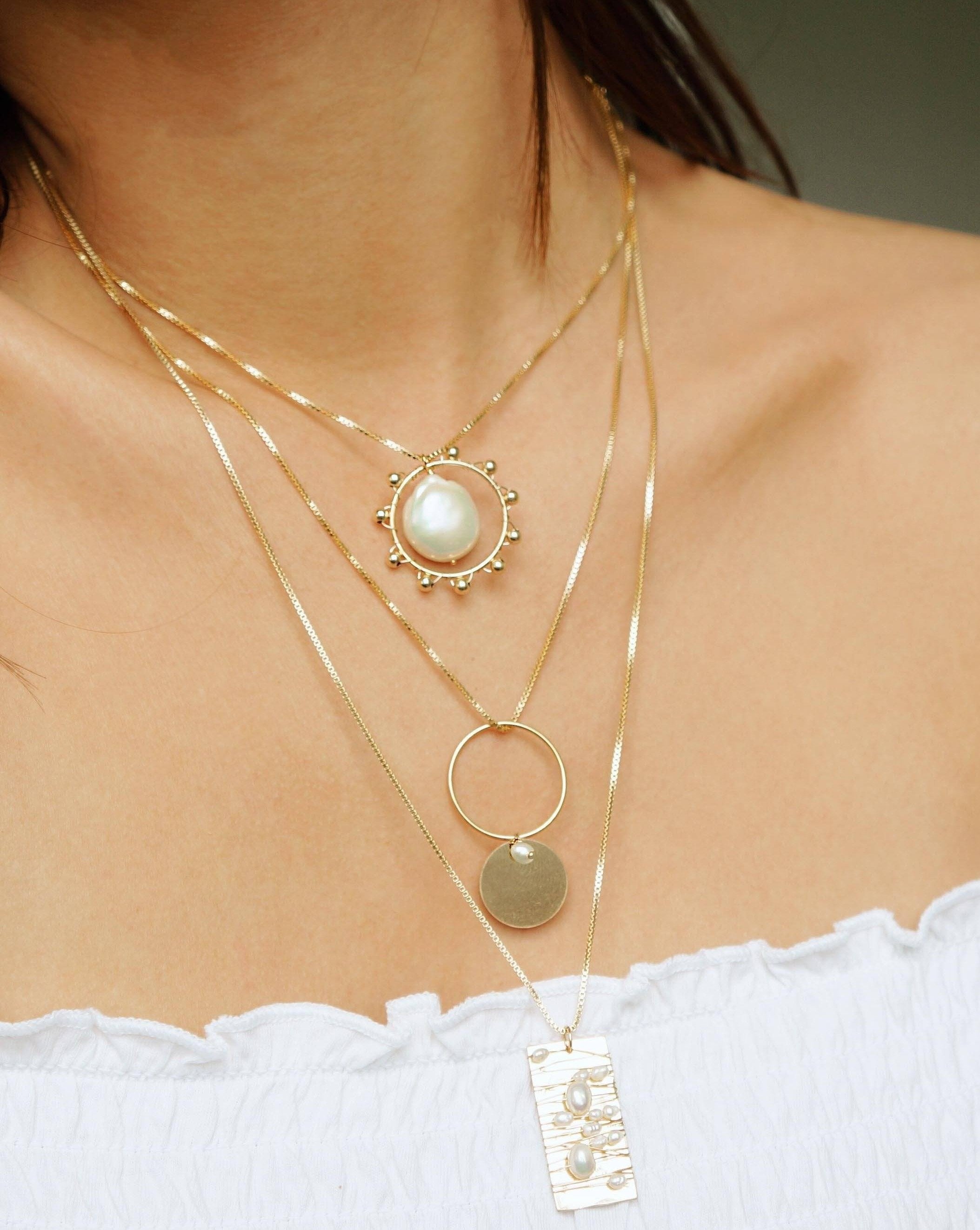 Tabla Necklace by KOZAKH. A 20 inches long necklace, crafted in 14K Gold Filled, featuring a 14x28mm flat rectangle medallion wrapped with white rice pearls and irregular white Pearls.