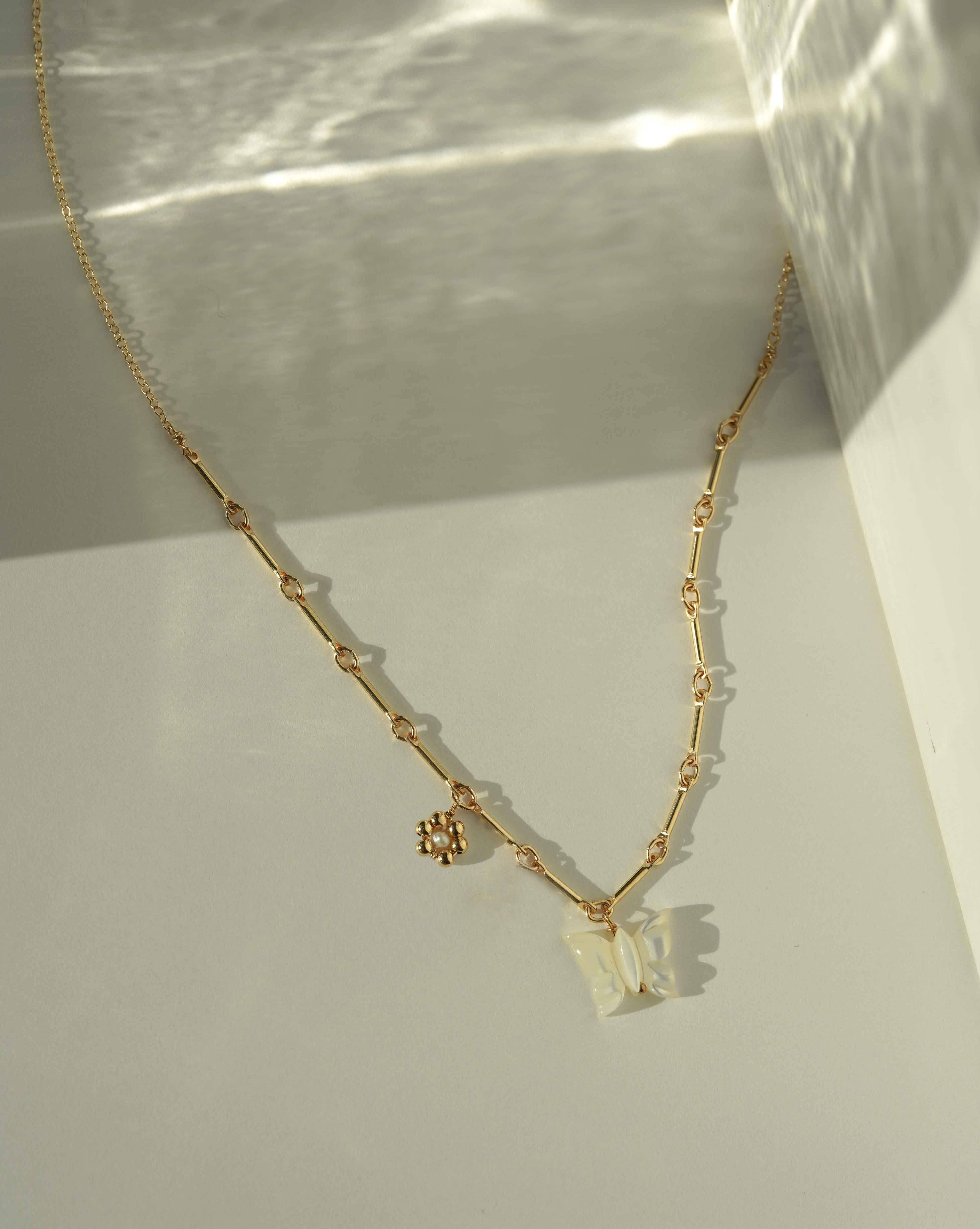 Tinley Necklace by KOZAKH. A 16 to 18 inch adjustable length necklace, with flat cable chain on top half and bar link chain on bottom half, crafted in 14K Gold Filled, featuring a hand-carved Mother of Pearl butterfly charm and a handmade gold beaded daisy with 2mm pearl in the center.