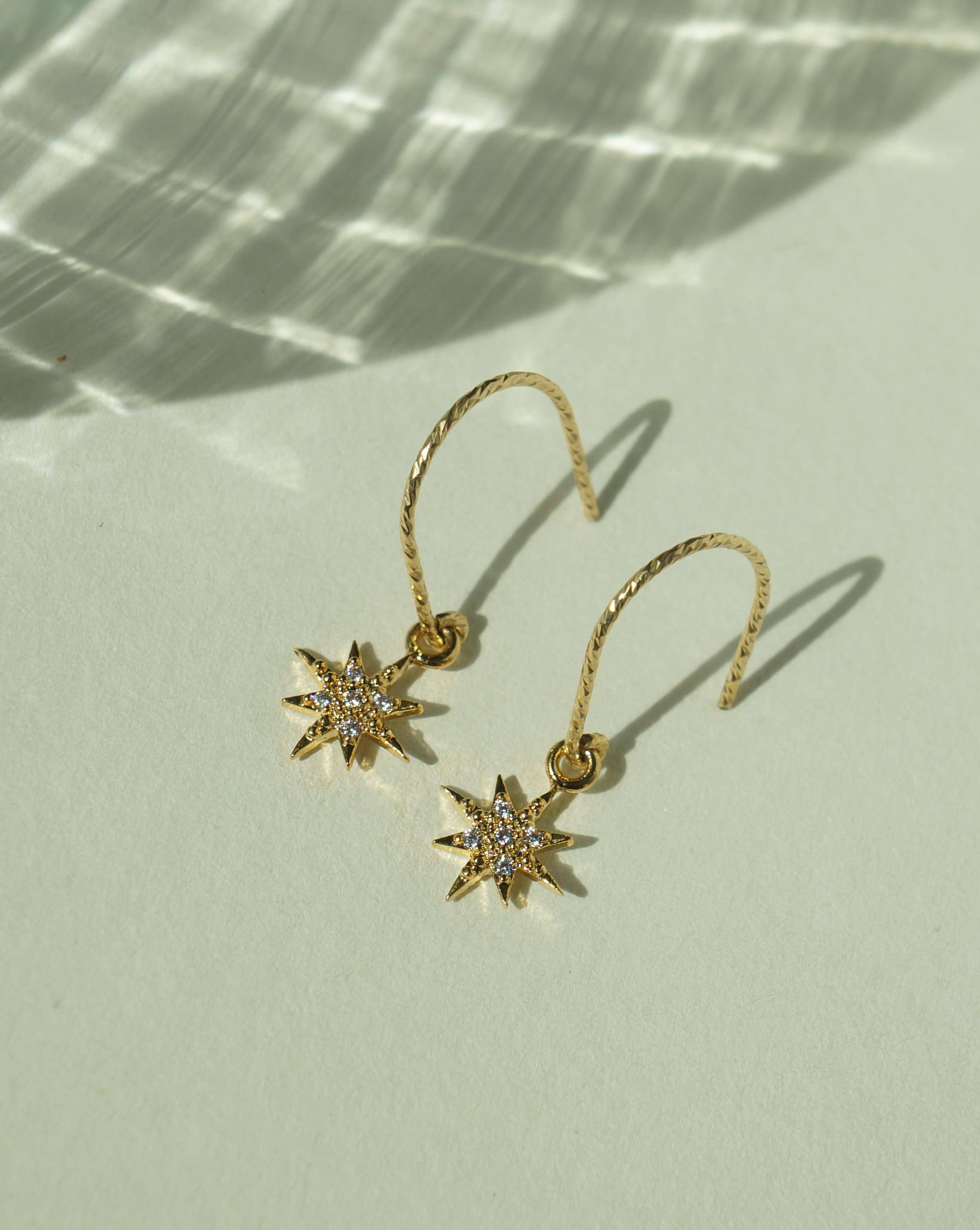 You Star Earrings by KOZAKH. Diamond textured hook earrings, crafted in 14K Gold Filled, featuring a Cubic Zirconia encrusted 8 point star charm.