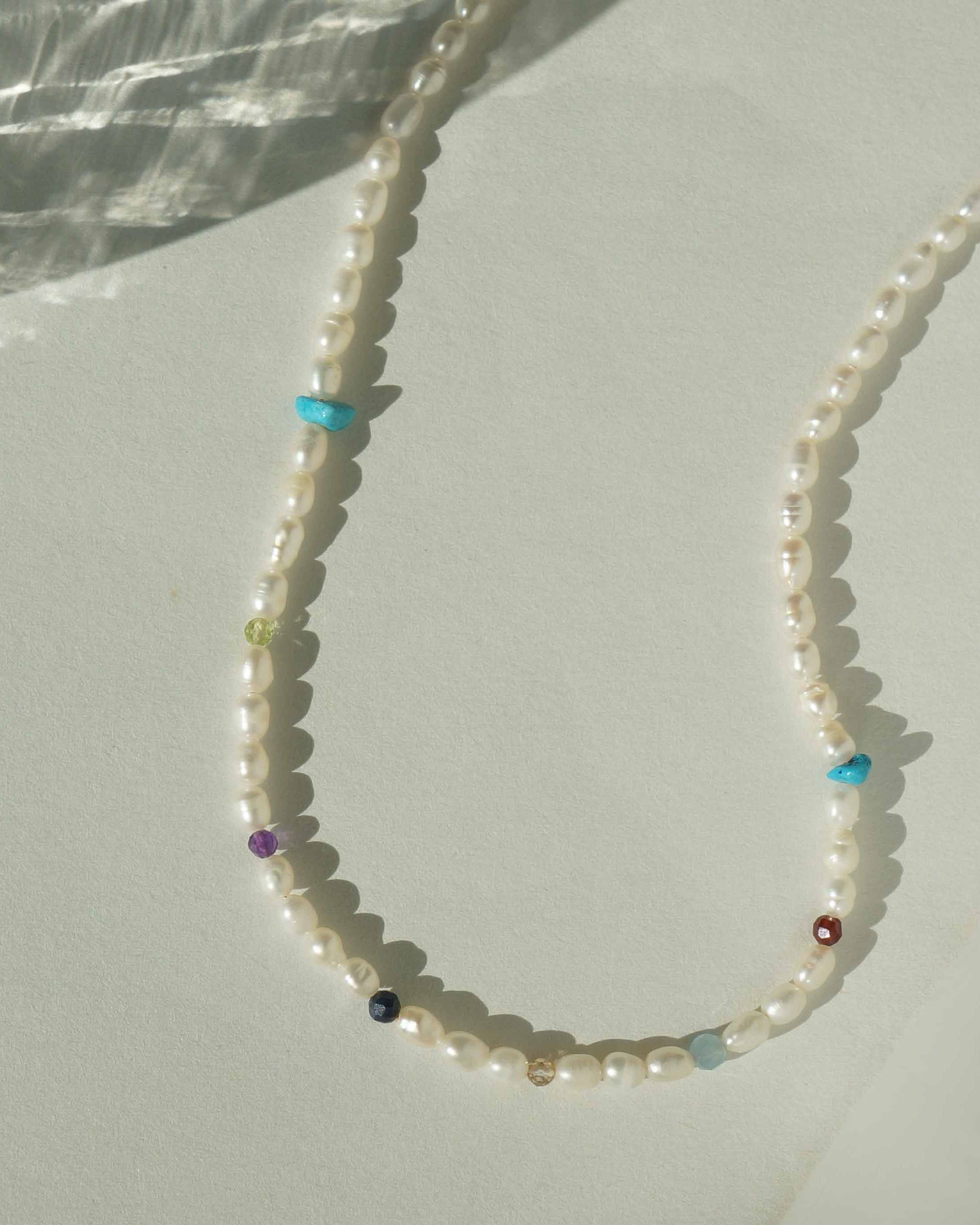 Zulema Necklace by KOZAKH. A 16 to 18 inch adjustable length, freshwater rice pearl strand necklace, clasp crafted in 14K Gold Filled, featuring Turquoise, Peridot, Sapphire, Topaz, Garnet, Aquamarine, and Amethyst gemstones.